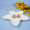 Pair of gold and pink earrings on a white starfish with yellow flowers on a blue background