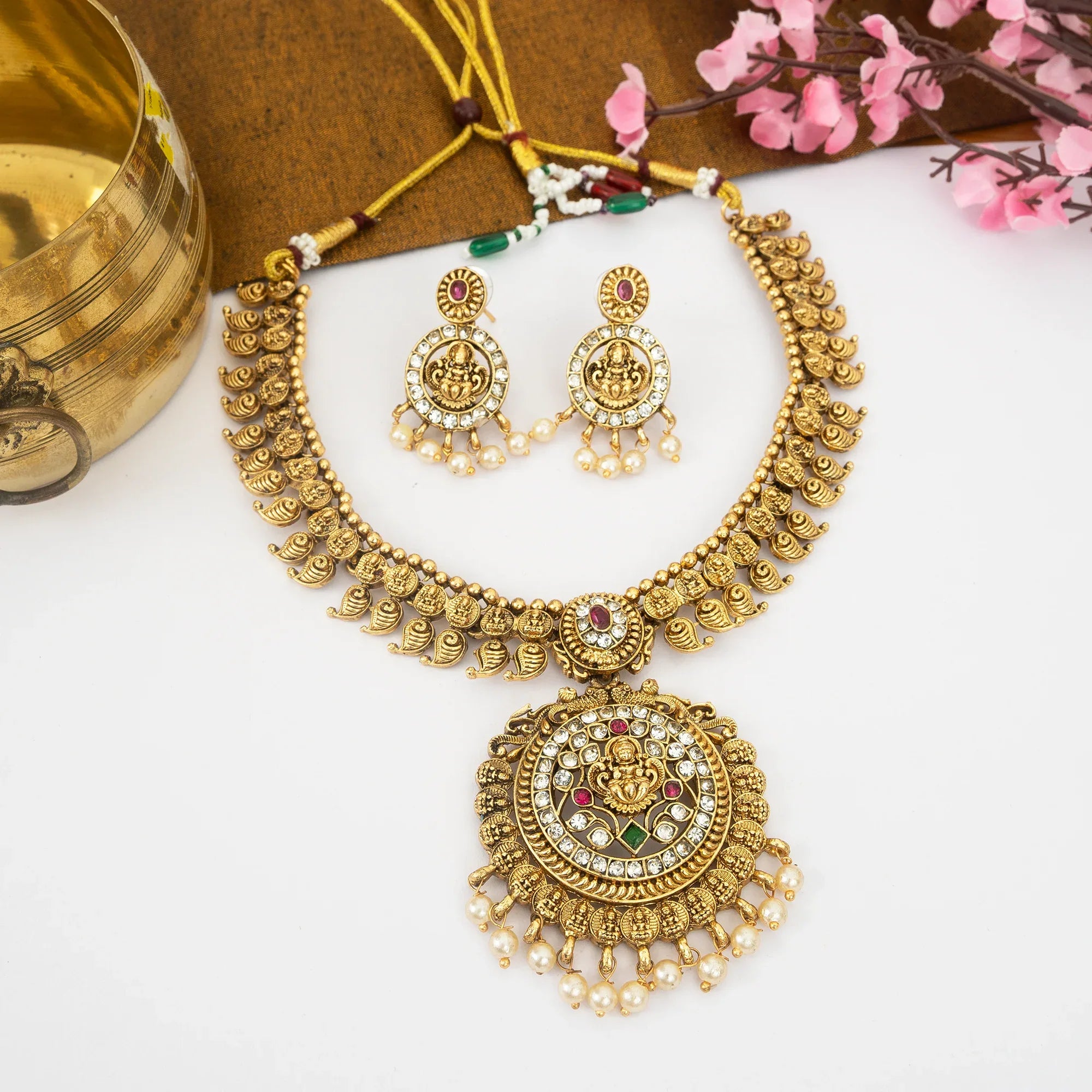 Gold necklace and earrings on a white surface with decorative elements.