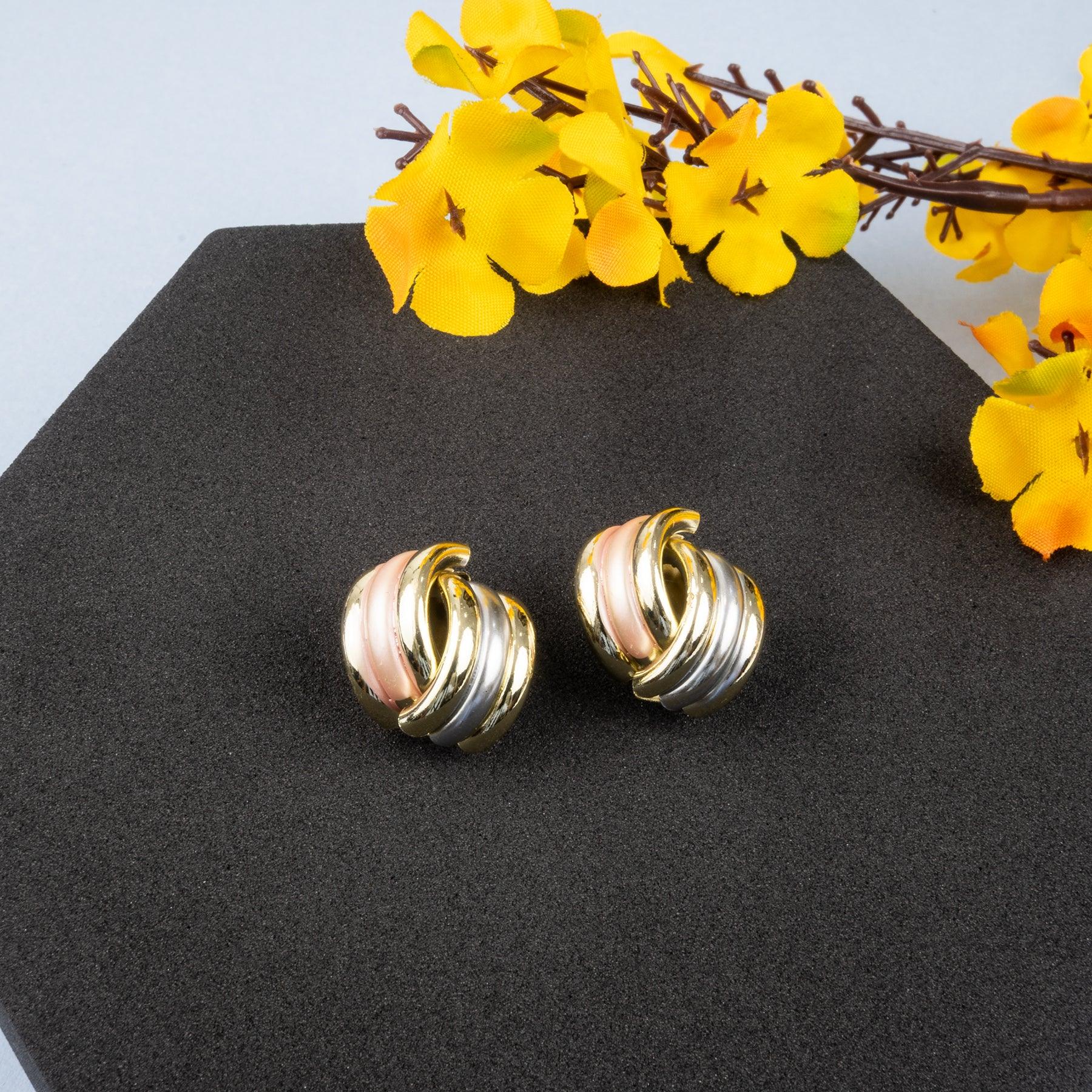 Tri-color gold earrings on a black stand with yellow flowers in the background