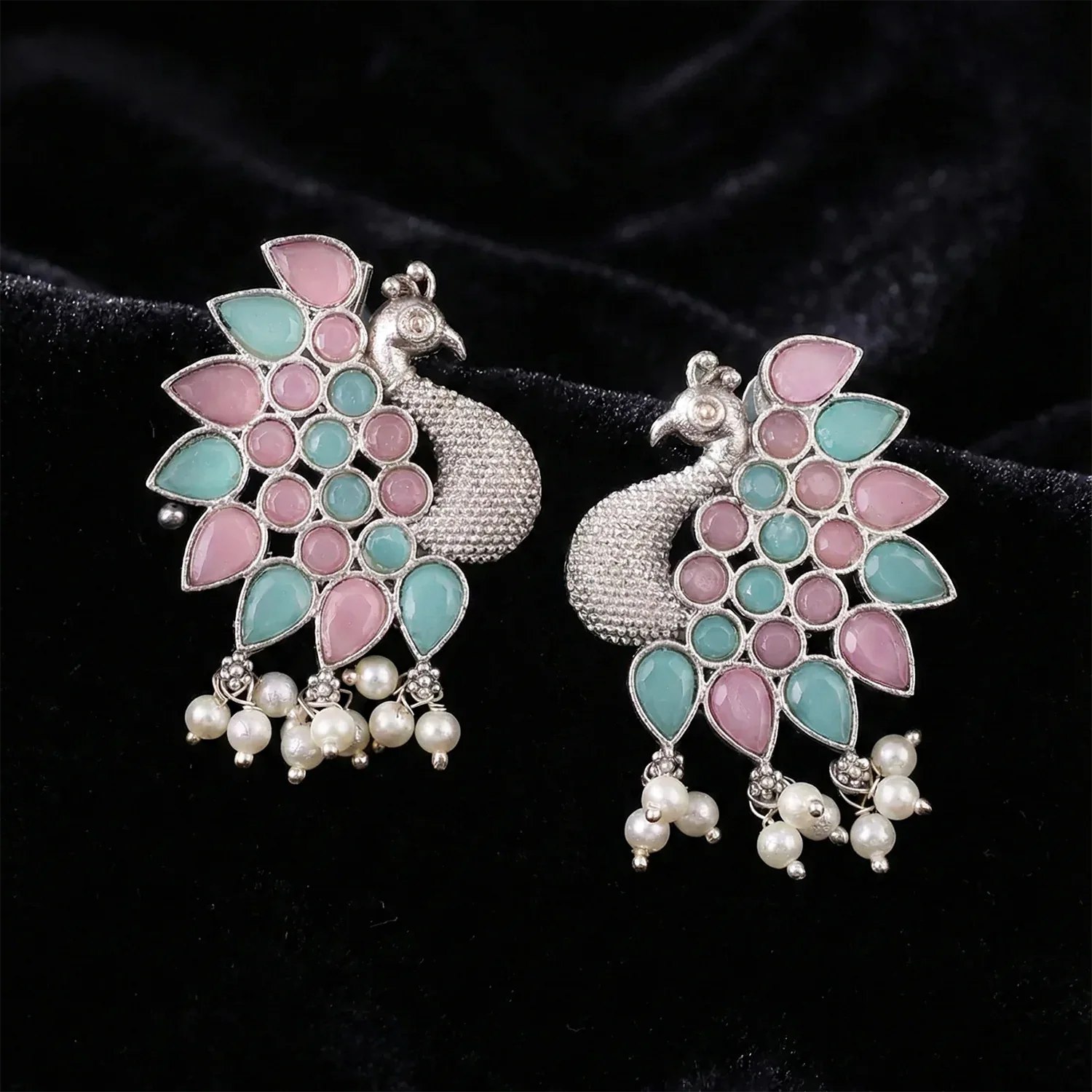 Peacock-shaped earrings with pink and blue stones on a black background