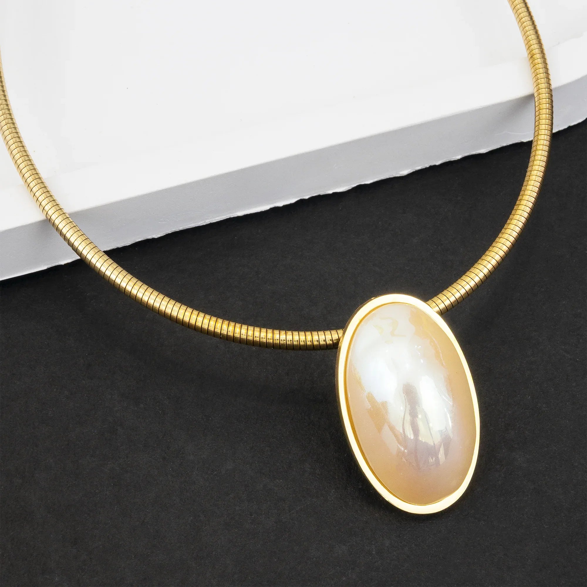 Gold necklace with a large, oval-shaped pearl pendant on a dark surface.
