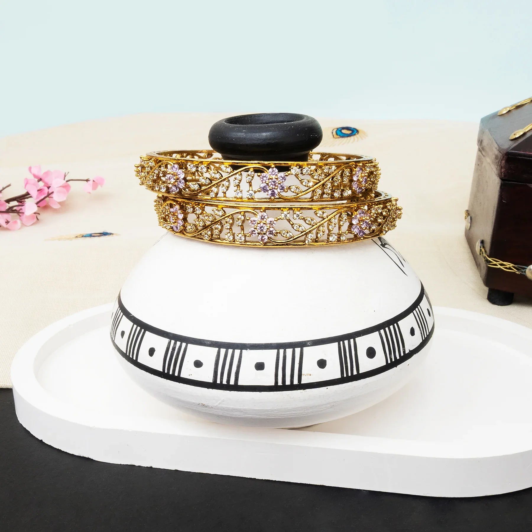 White vase with black patterns holding gold and silver bracelets on a white surface.