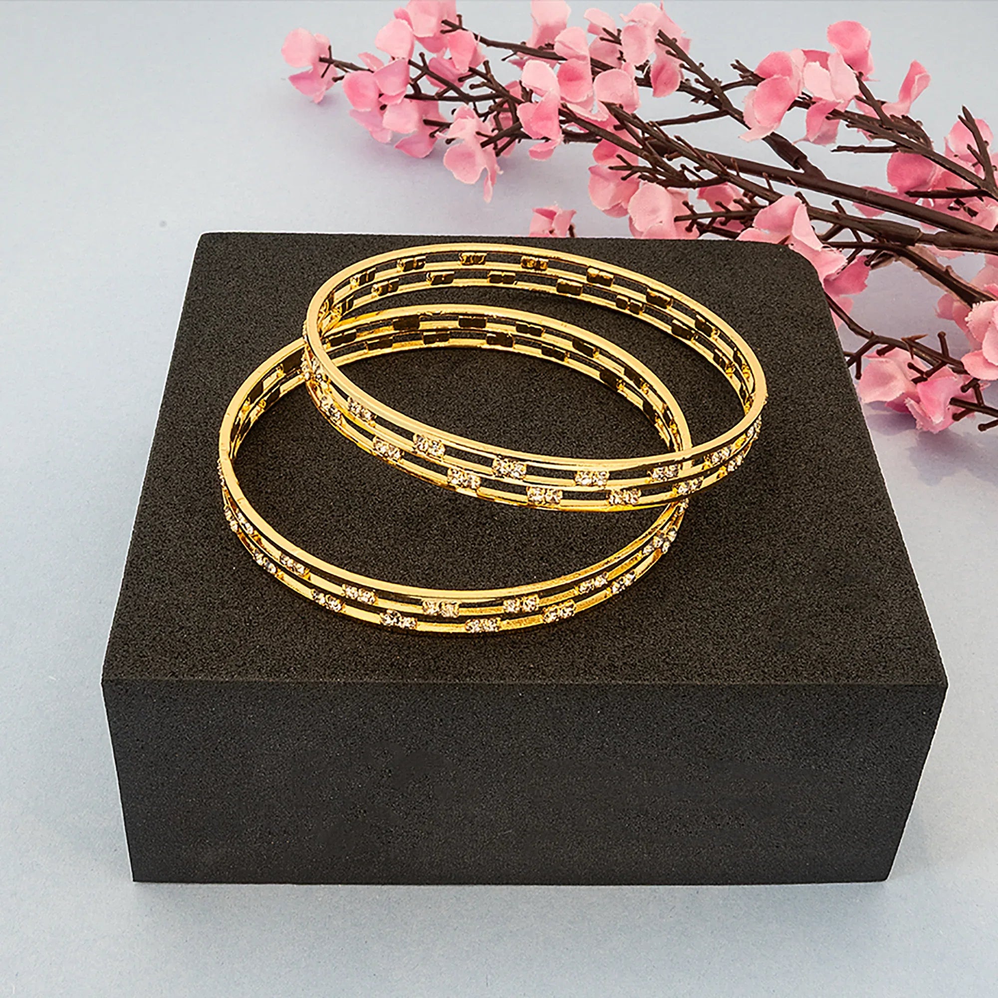Gold bangles on a black box with pink flowers in the background