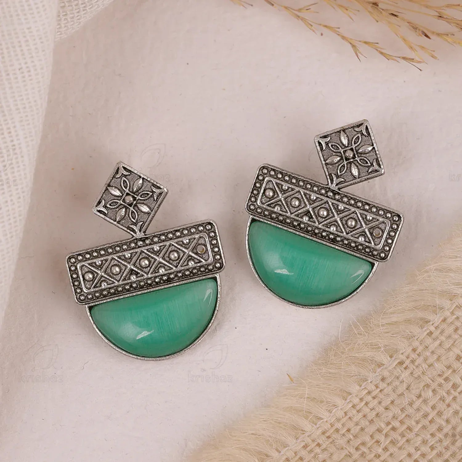 Pair of earrings with turquoise stones and silver floral patterns on a textured beige surface.