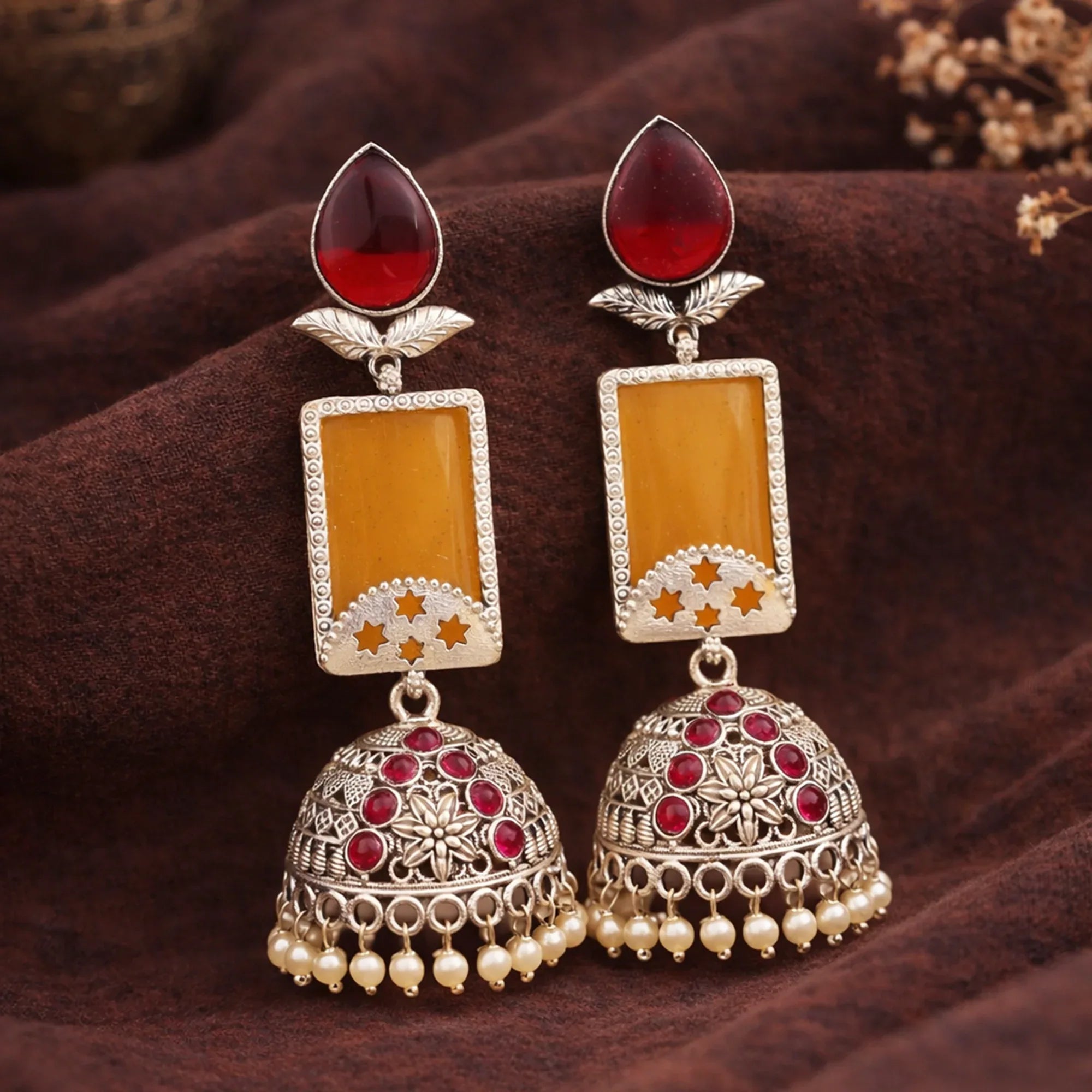 Ornate earrings with red and yellow stones on a brown fabric background