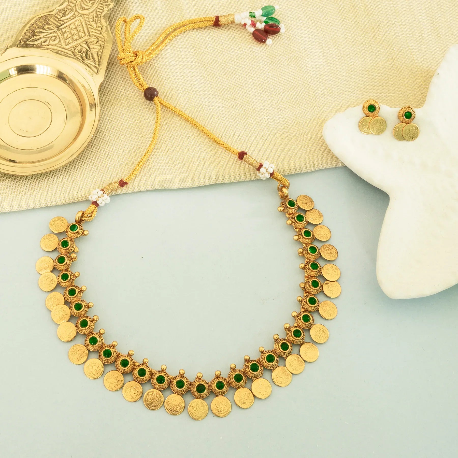 Gold necklace with green stones on a light surface