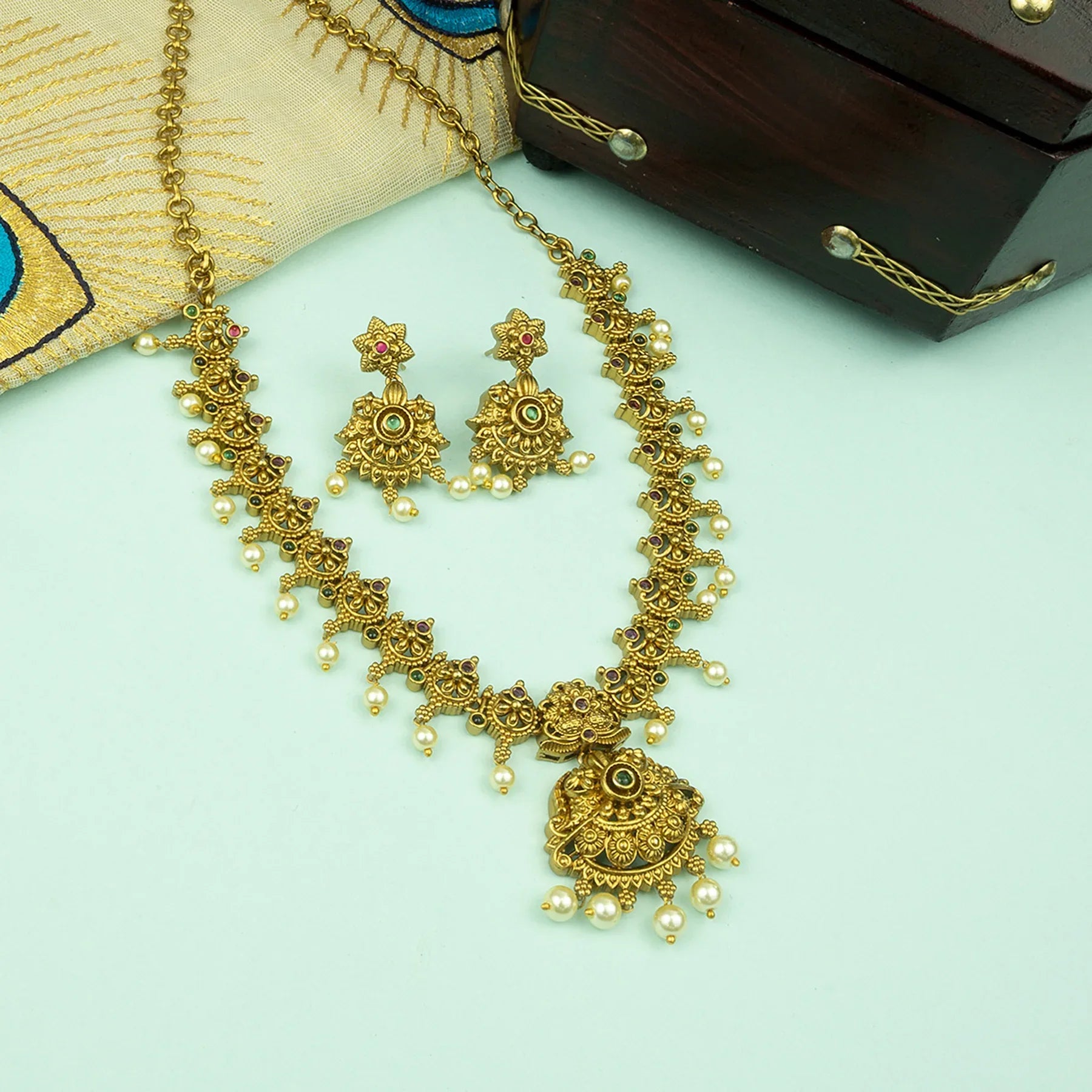 Gold necklace and earrings on a light blue surface with a wooden box in the background.