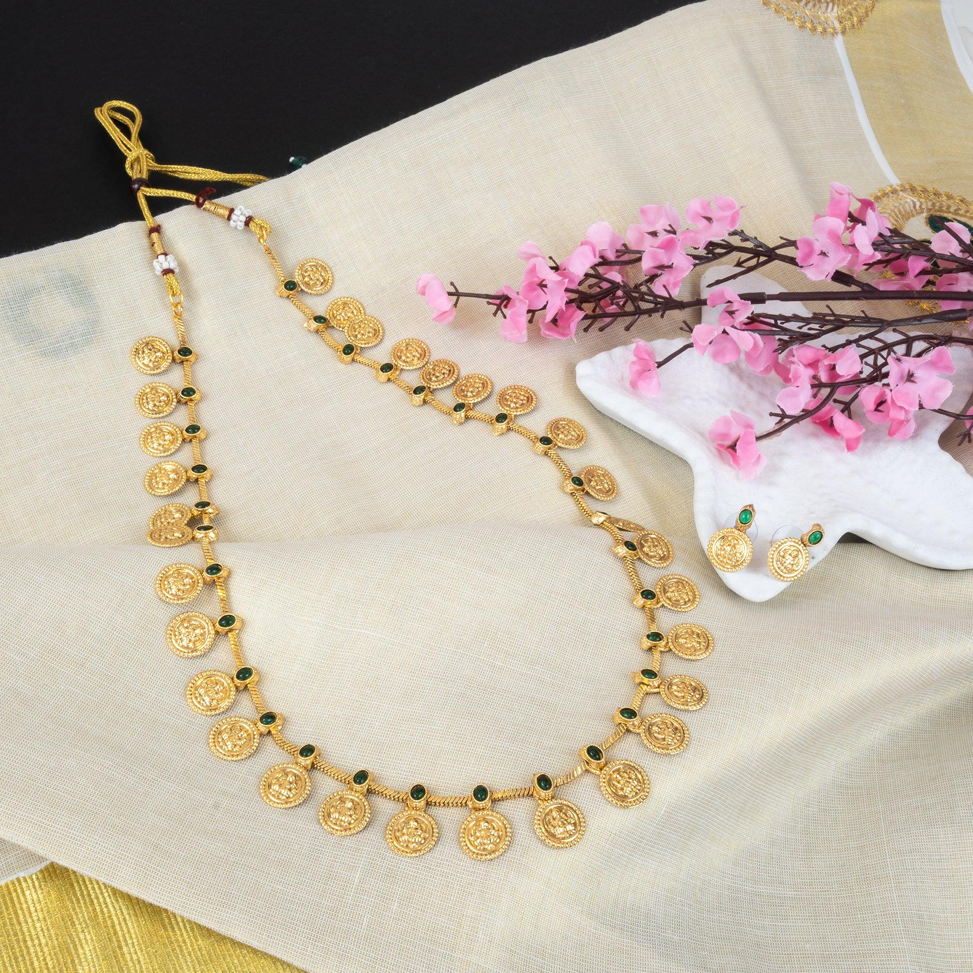 Gold necklace with coin-like designs on a beige fabric background with pink flowers.