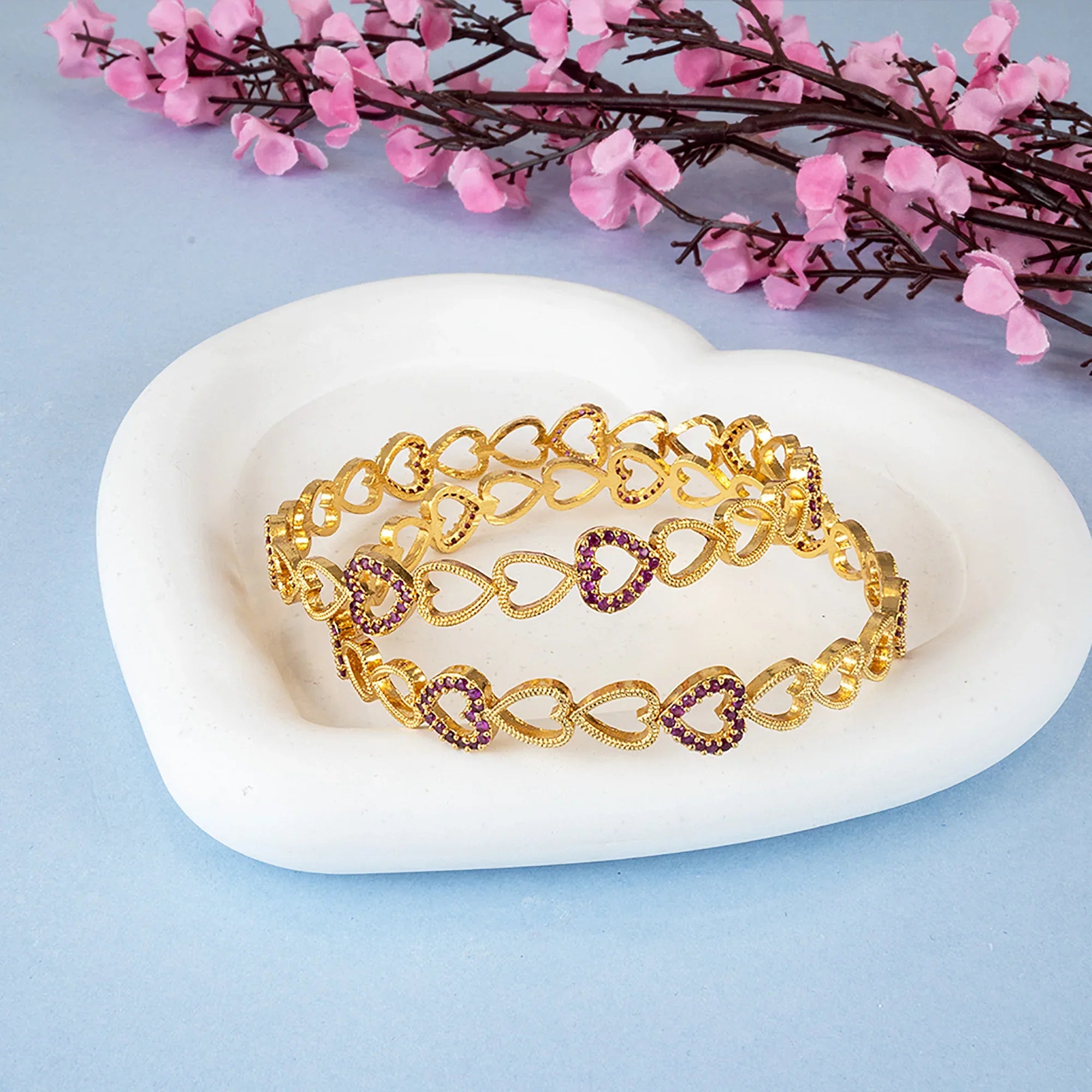 Gold bracelet with purple stones on a white stone surface with pink flowers in the background