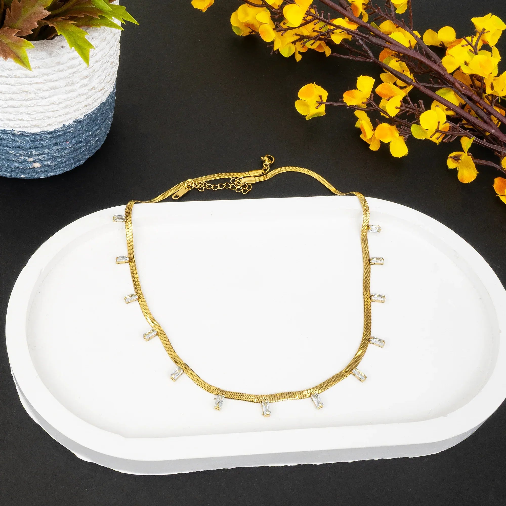 Gold necklace with small pearls on a white dish with yellow flowers in the background