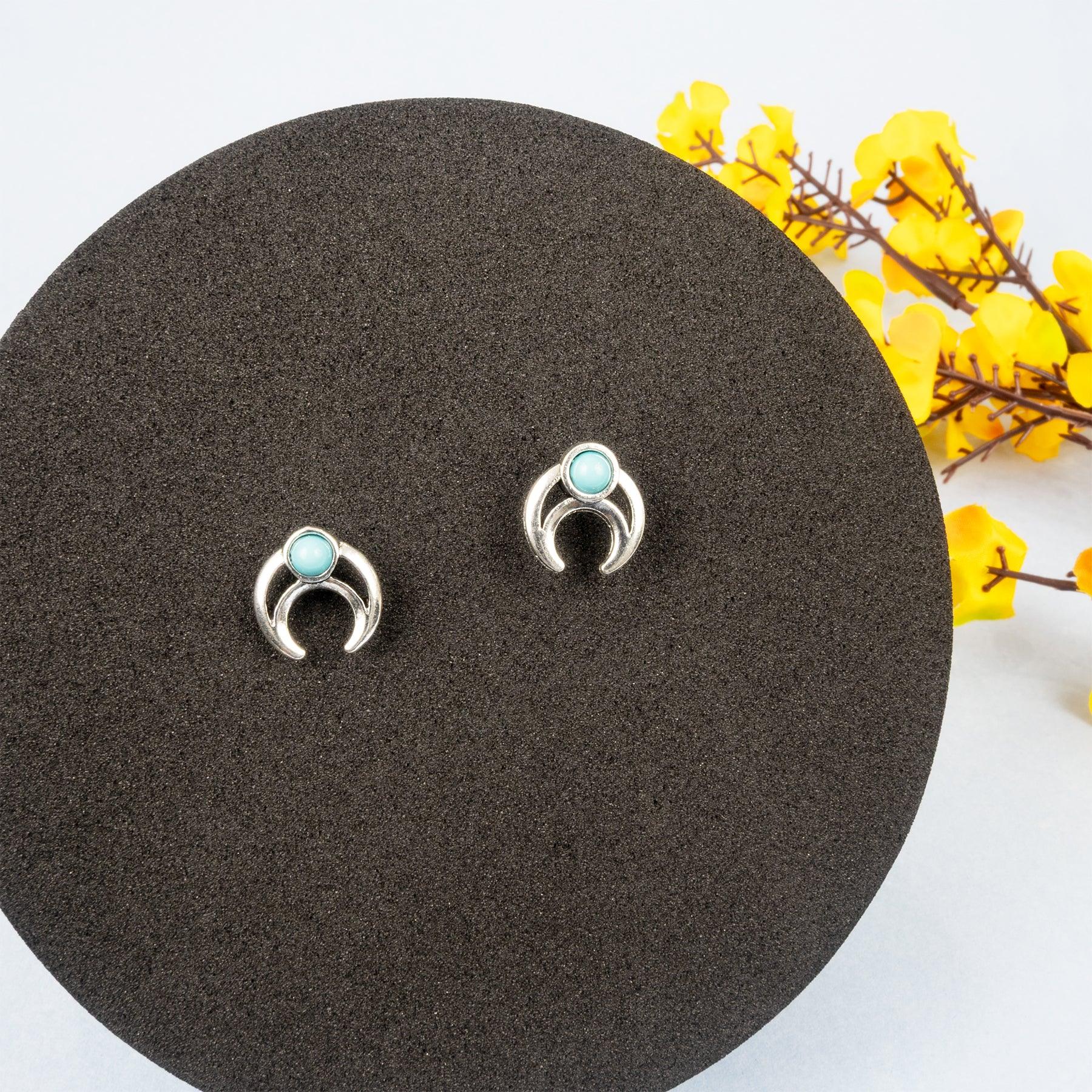 Silver earrings with turquoise stones on a dark brown stand with yellow flowers in the background