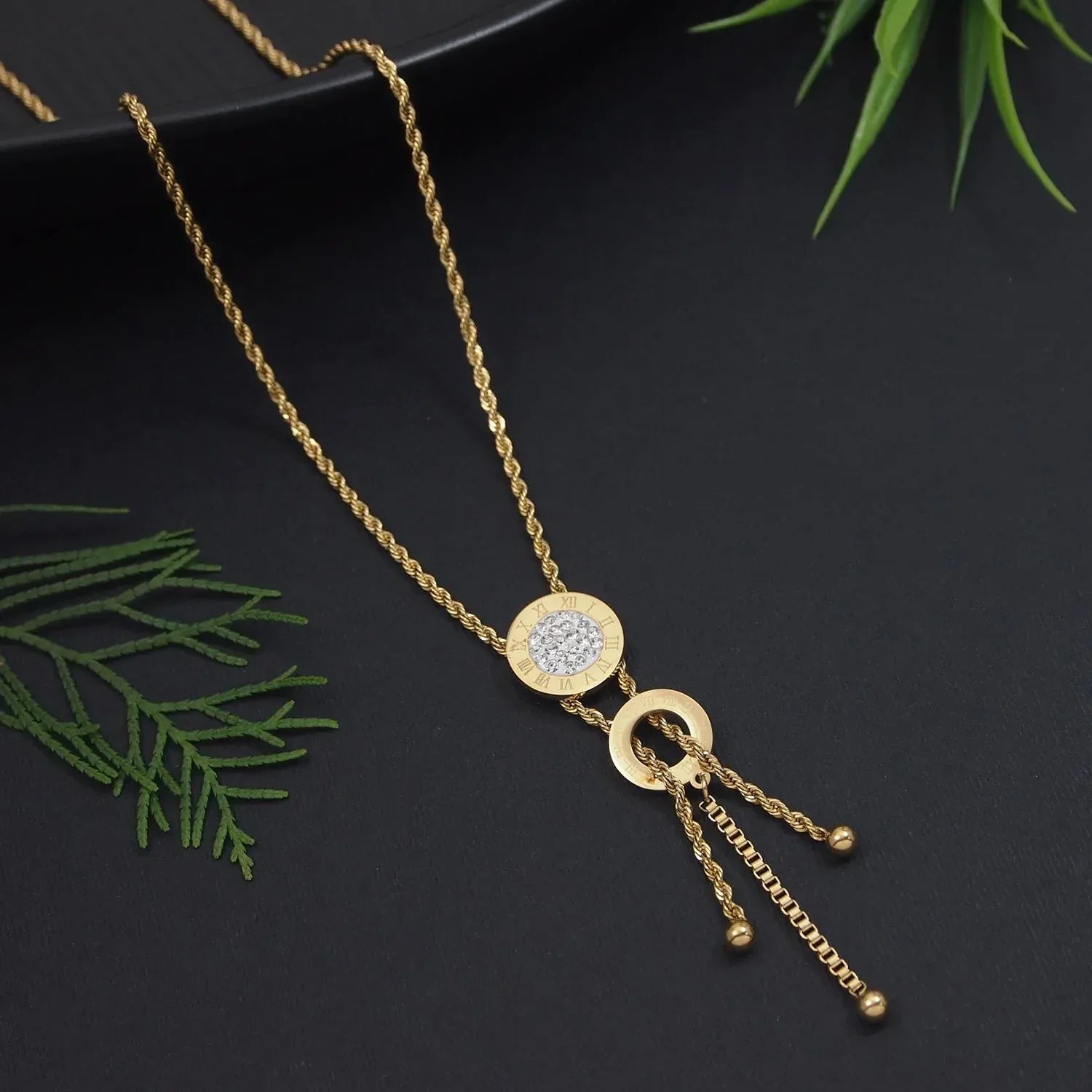 Gold necklace with pendant on a dark surface with green leaves