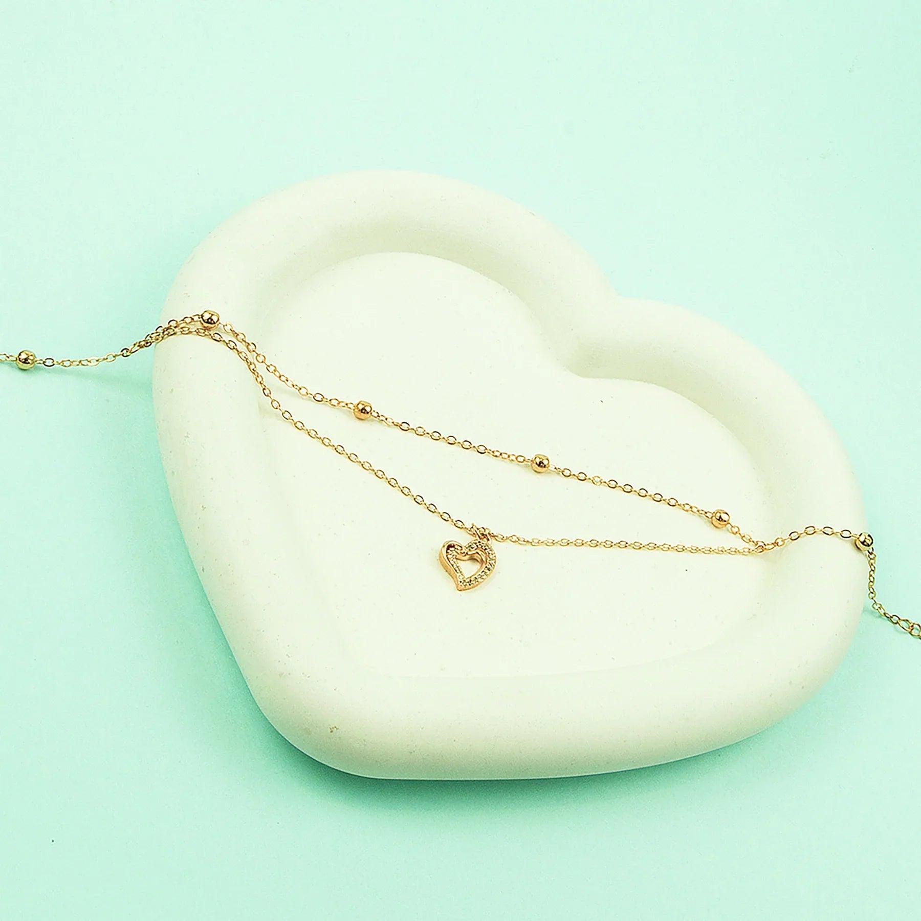 Gold necklace with a heart pendant on a white stone against a light green background