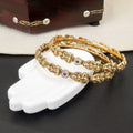 Gold bracelets with intricate designs on a white mannequin hand against a dark background