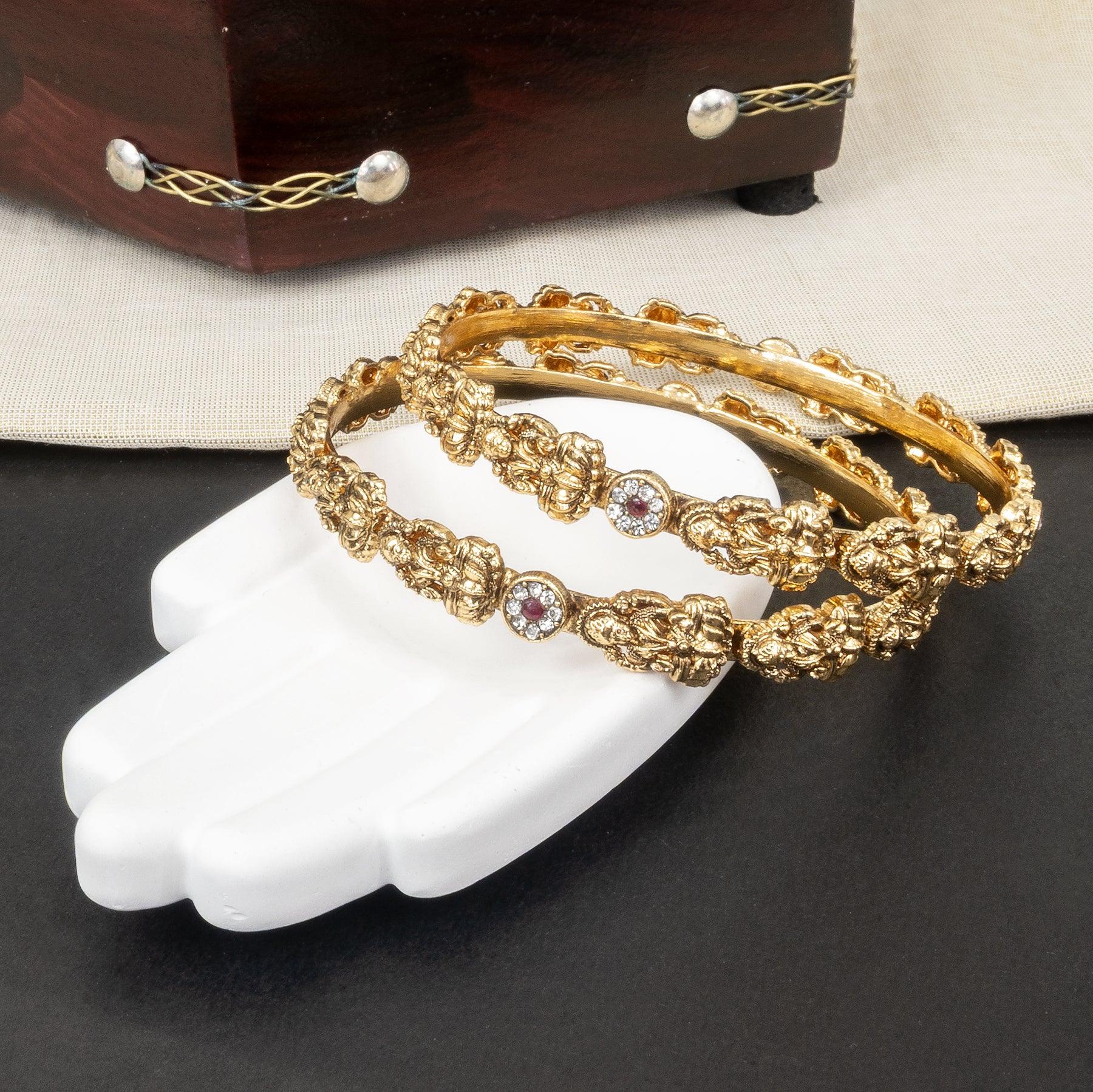Gold bracelets with intricate designs on a white mannequin hand against a dark background