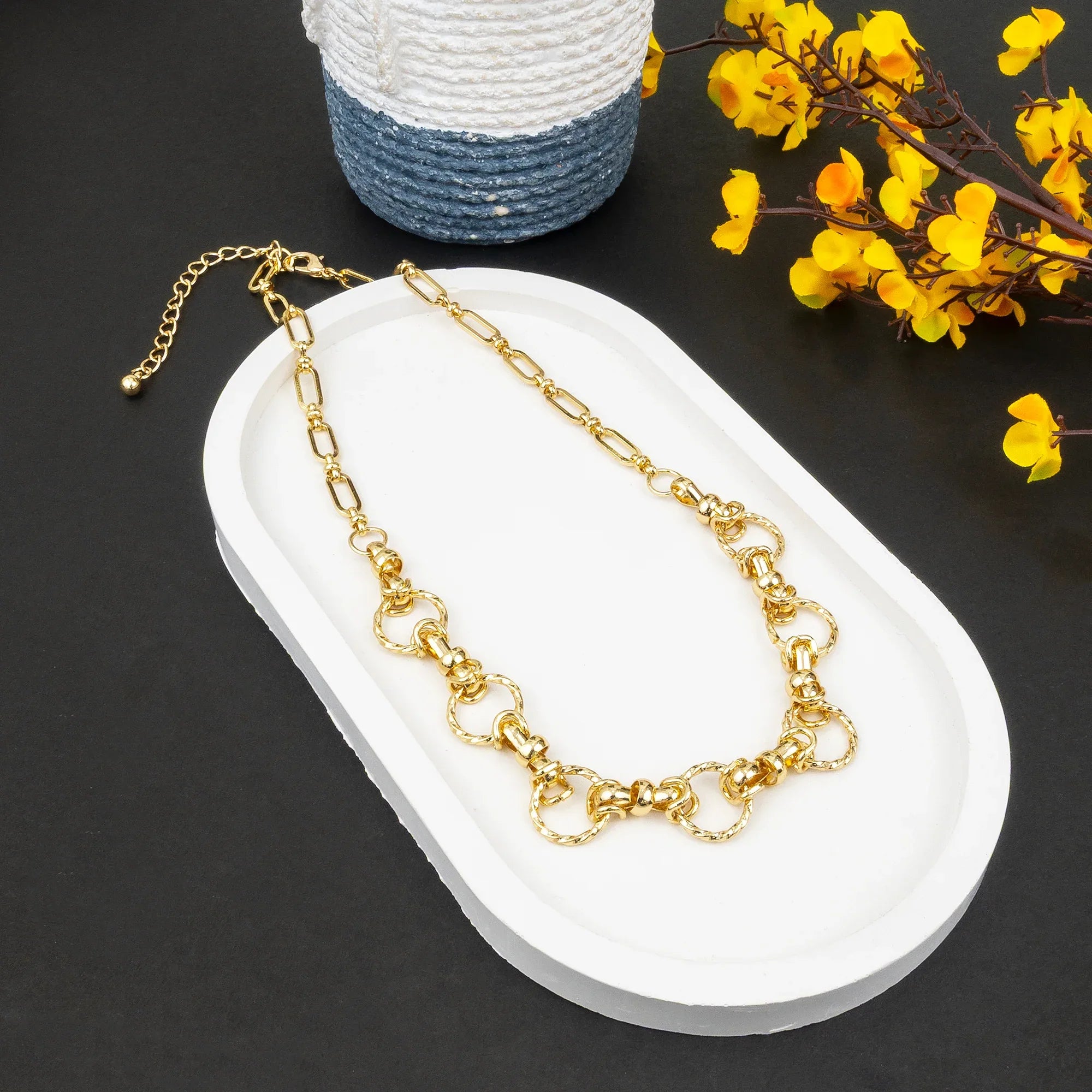 Gold chain necklace on a white stand with yellow flowers in the background