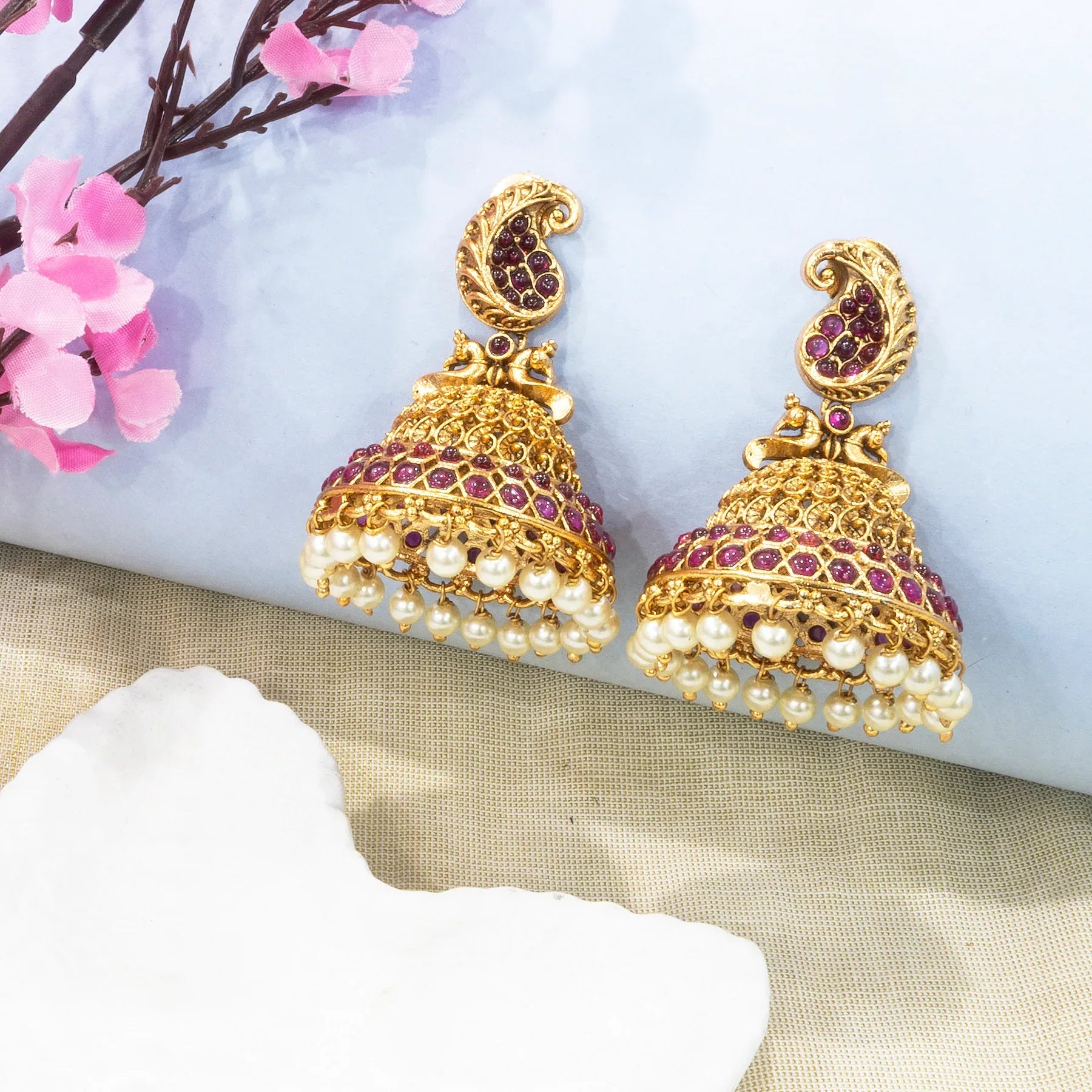 Gold and pearl earrings with red stones on a decorative background with flowers.