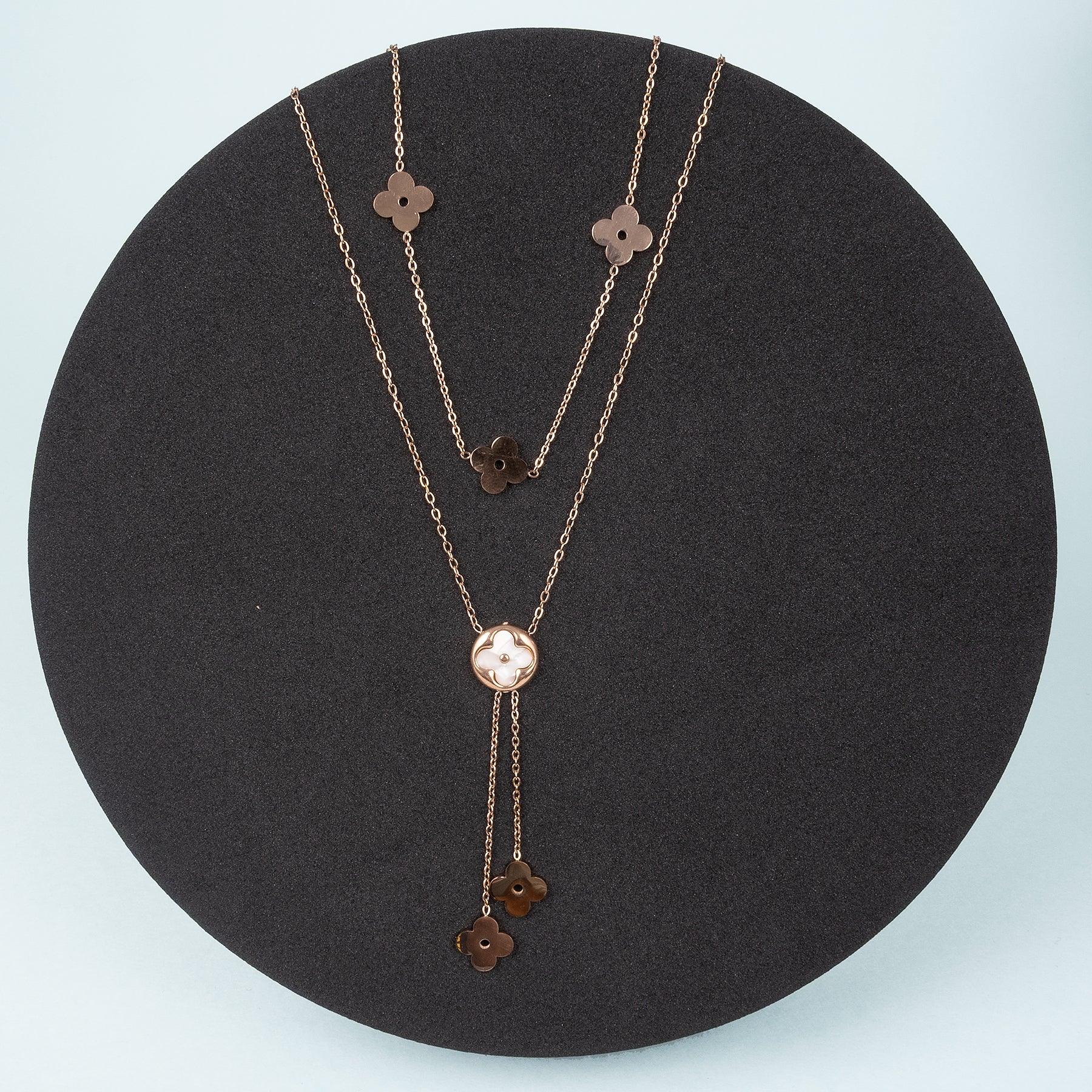 Rose gold necklace with floral pendants on a black circular stand against a light blue background