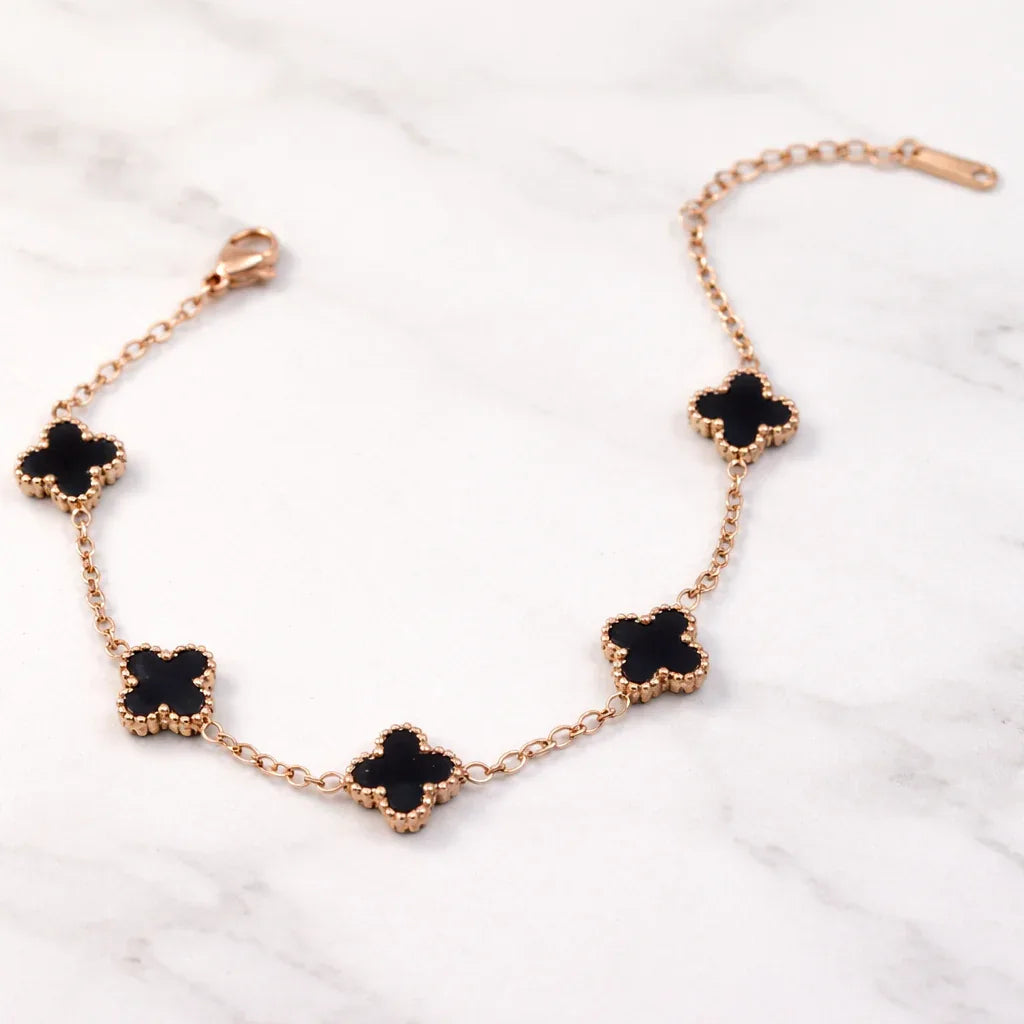 Rose gold bracelet with black clover-shaped charms on a white marble background