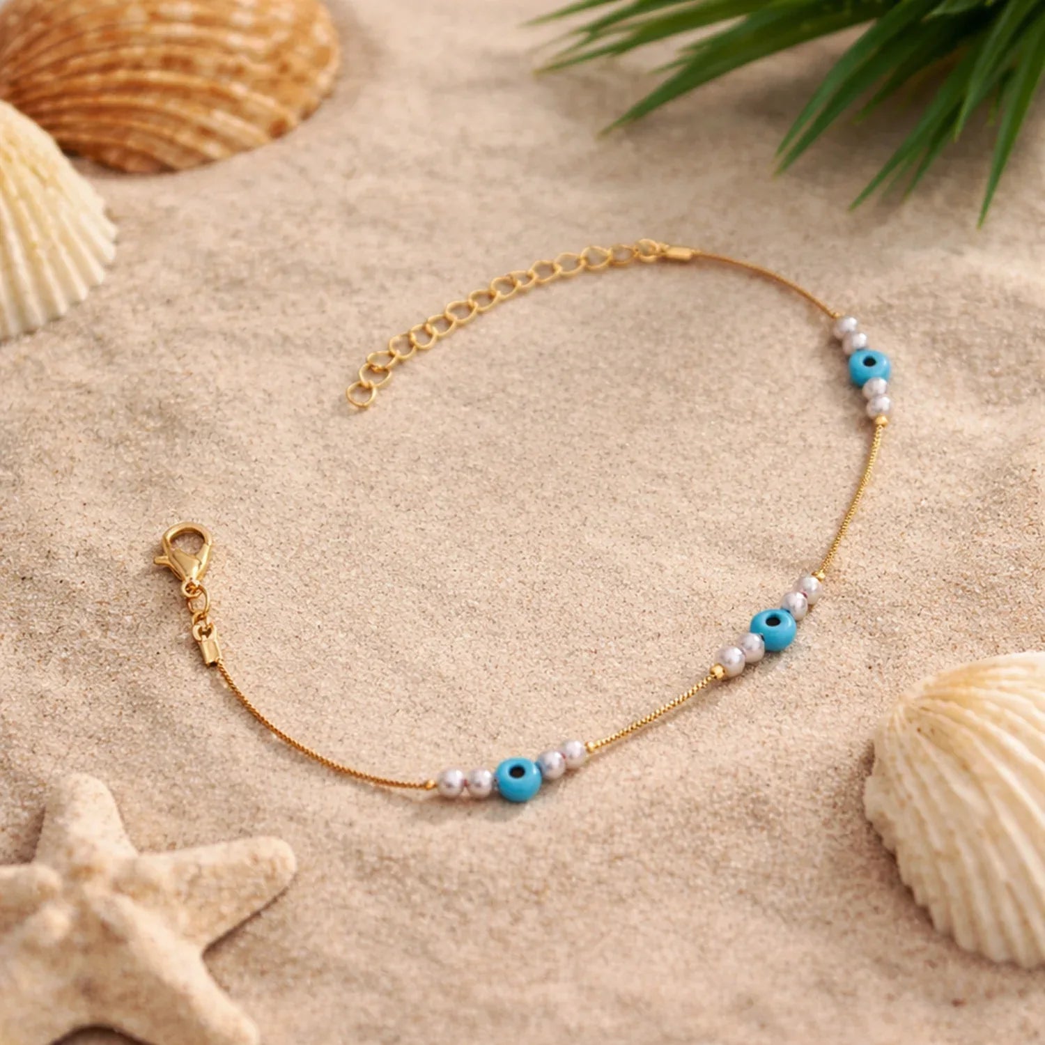 Gold bracelet with blue and white beads on sand with shells and starfish
