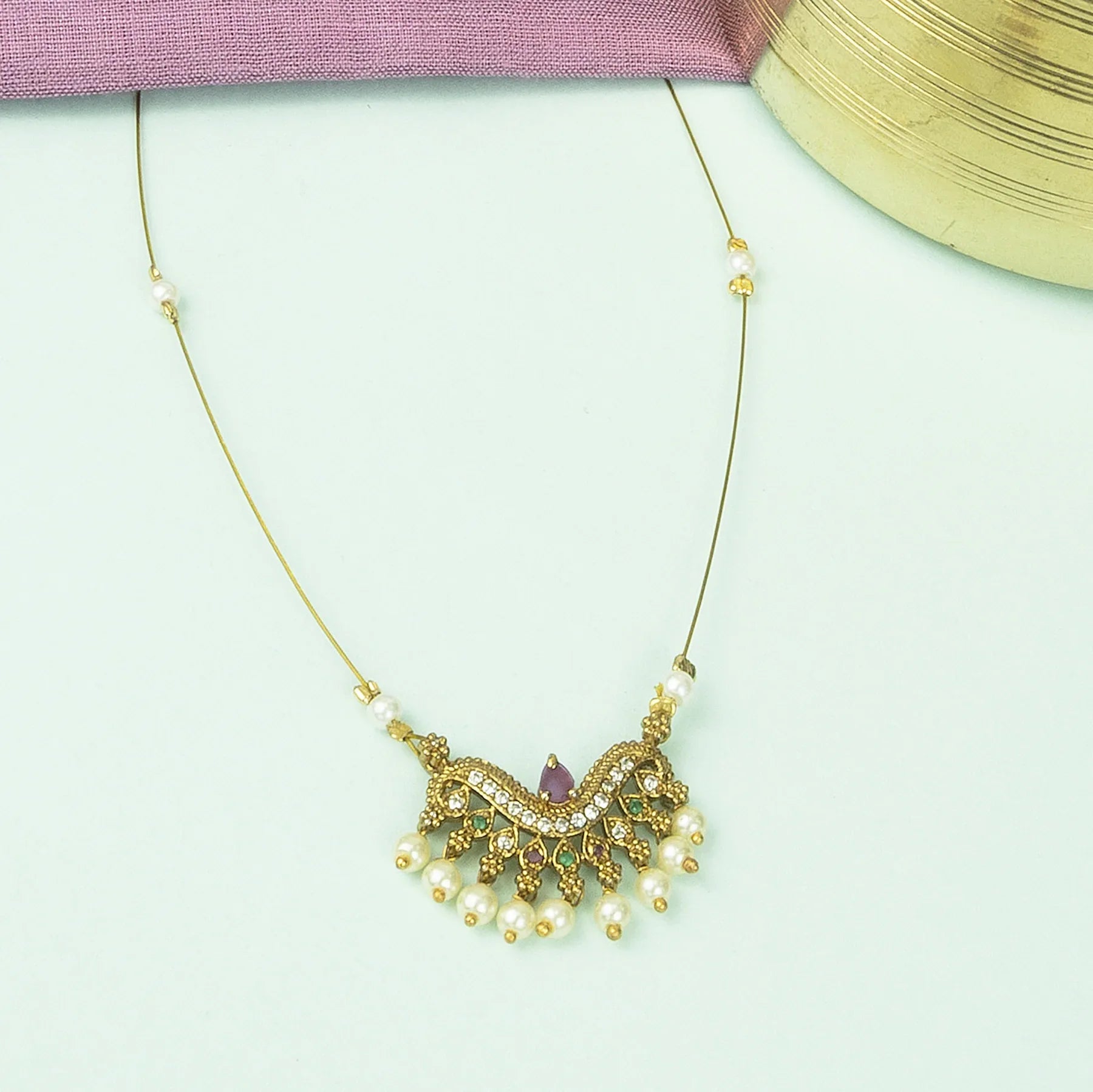 Decorative necklace with pearls and gold accents on a light green background