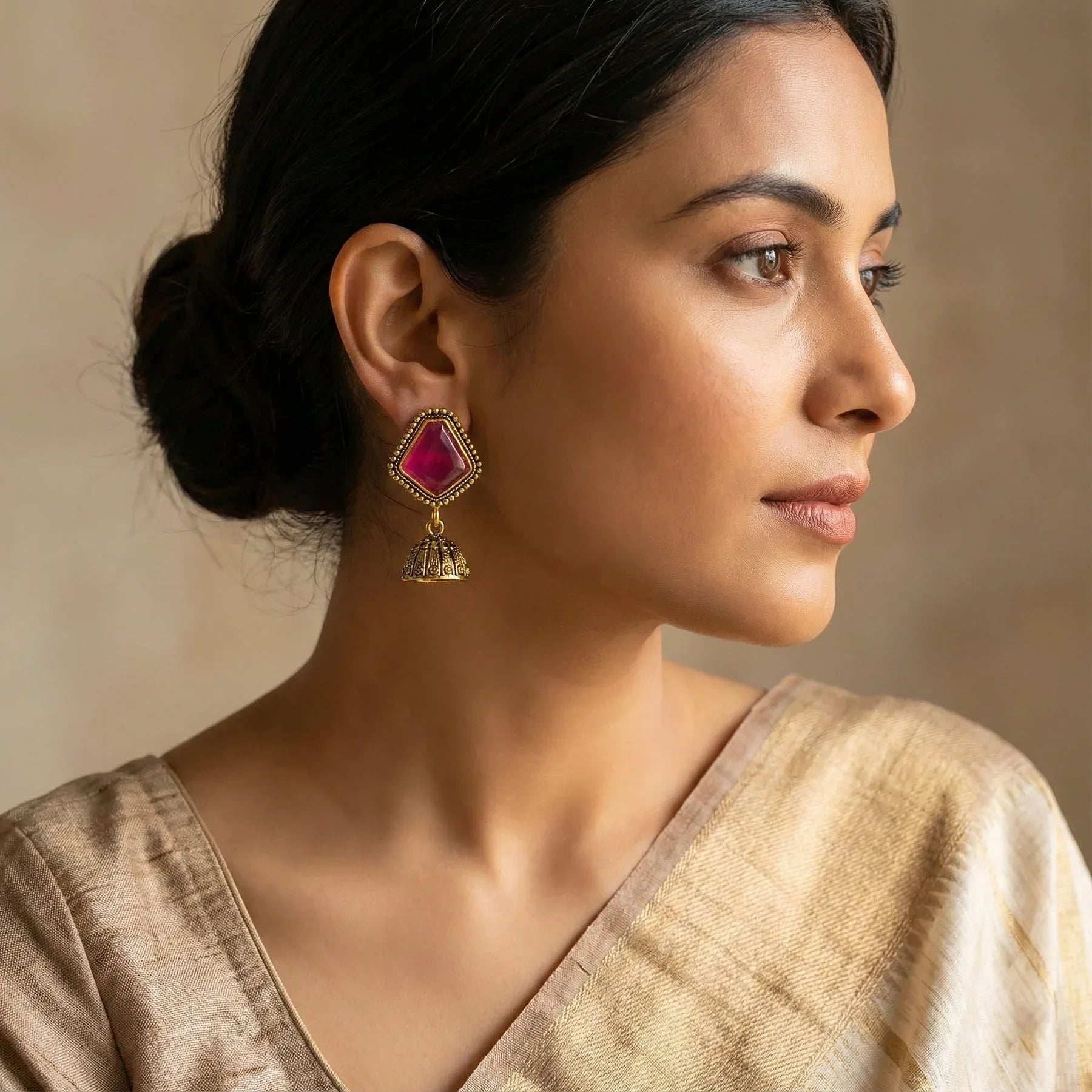 Woman wearing a gold and red earring with a beige background