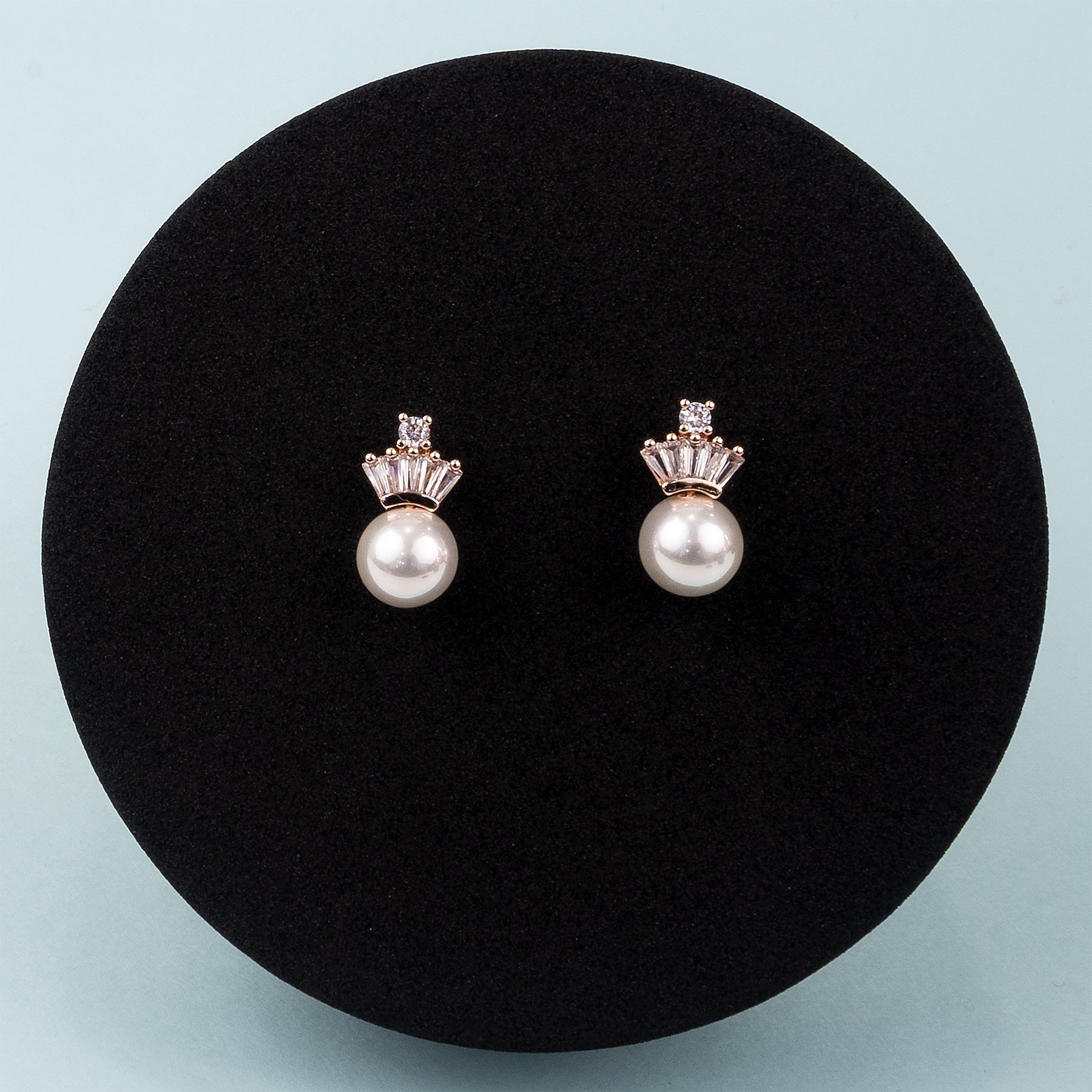 Pair of pearl earrings with rose gold settings on a black cushion against a light blue background