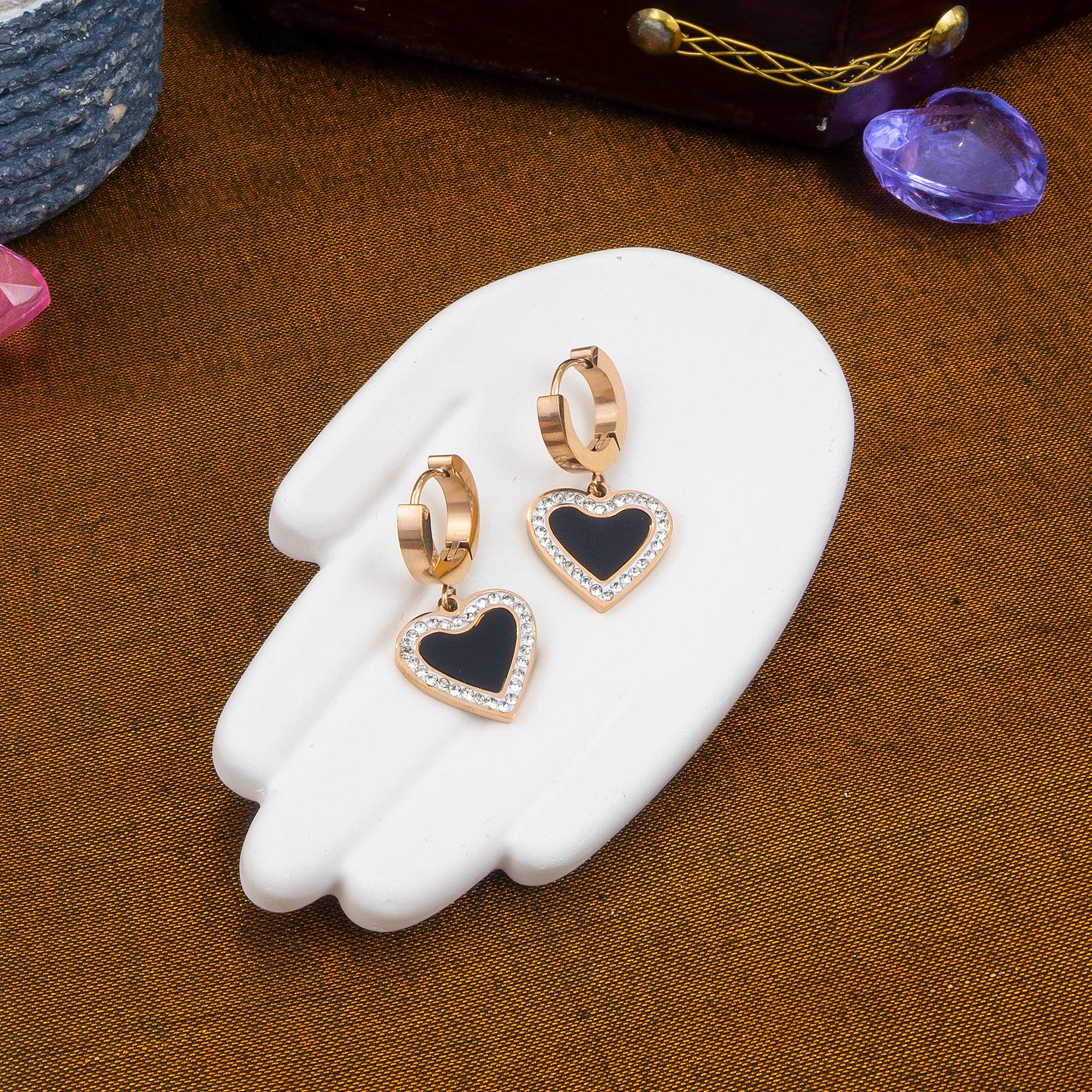 Heart-shaped earrings with black centers and gold accents on a white stand against a brown background.