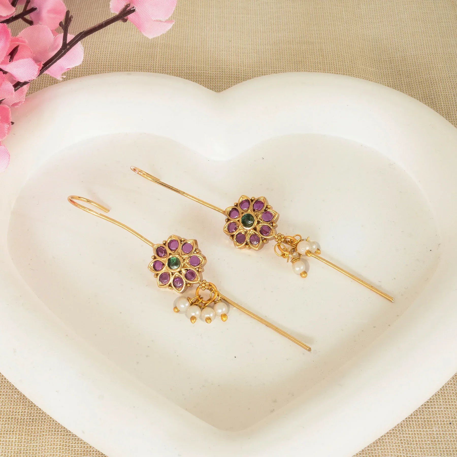 Gold hairpins with floral designs and gemstones on a heart-shaped white dish.