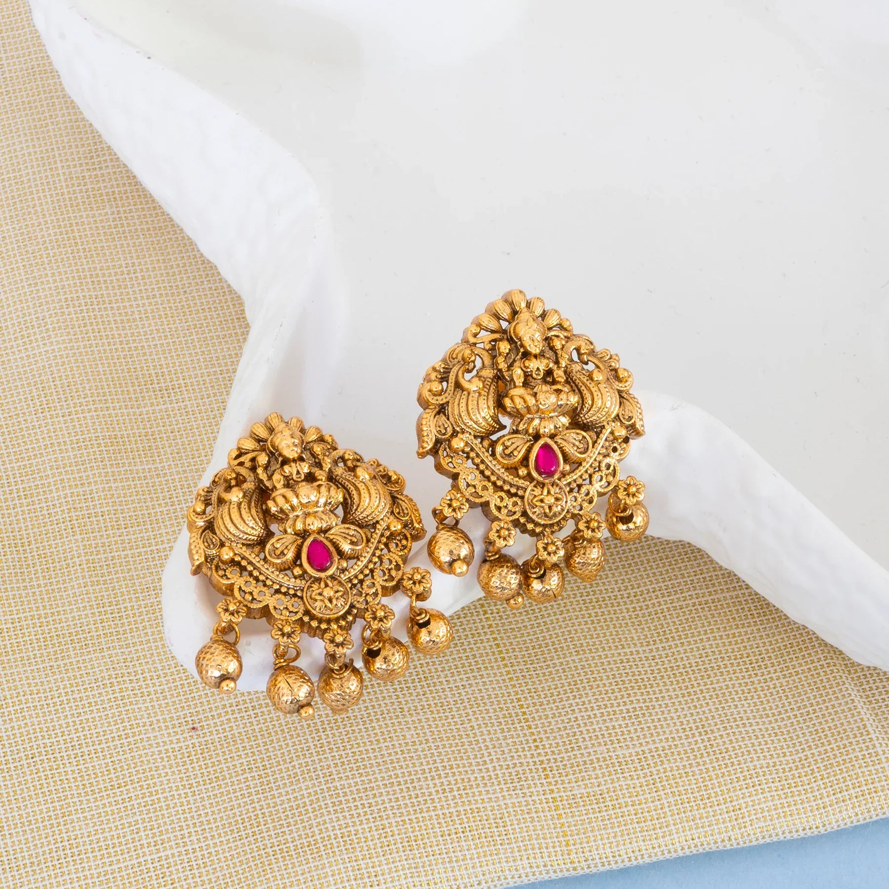 Gold earrings with red gemstones on a textured surface