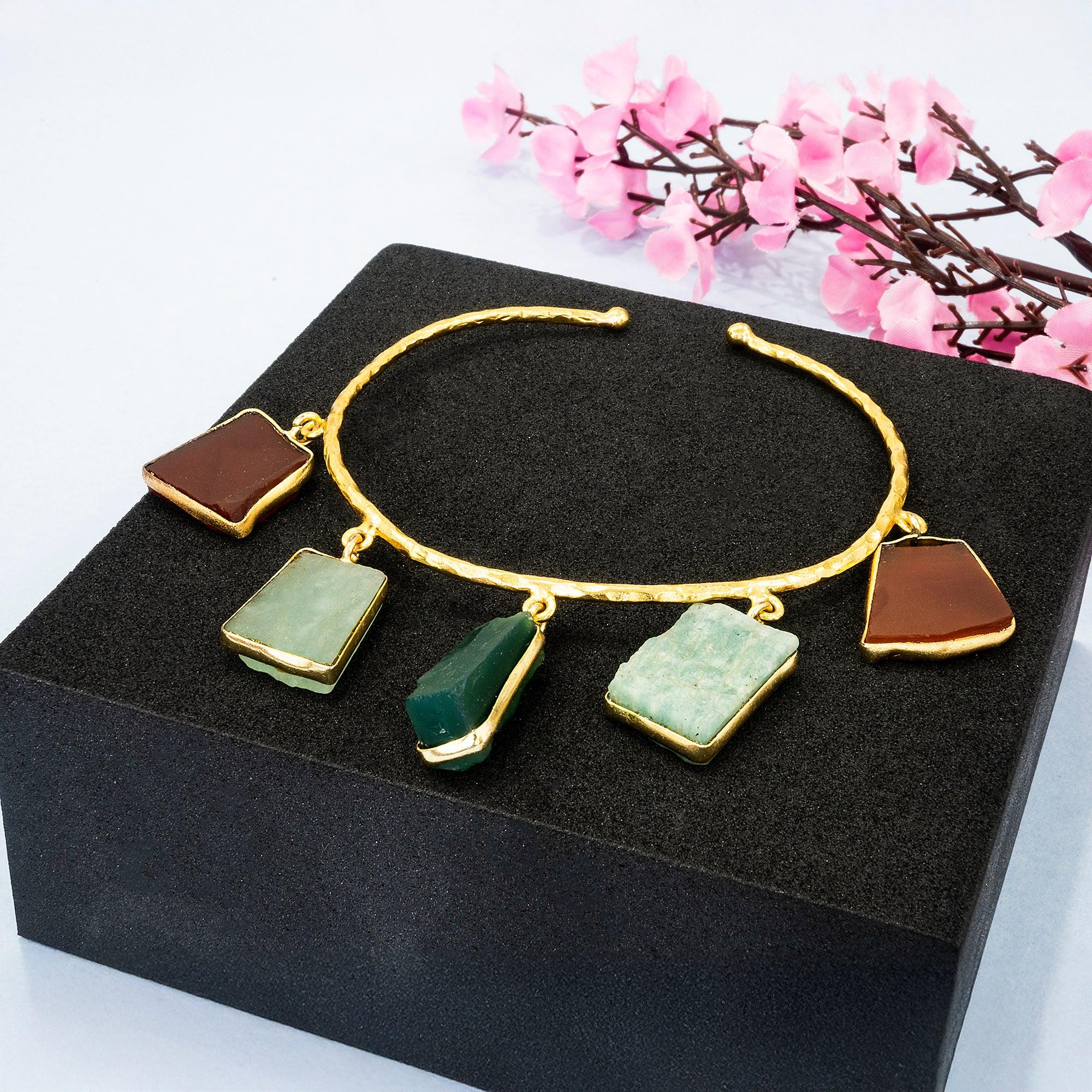 Gold bracelet with stone charms on a black box with pink flowers in the background
