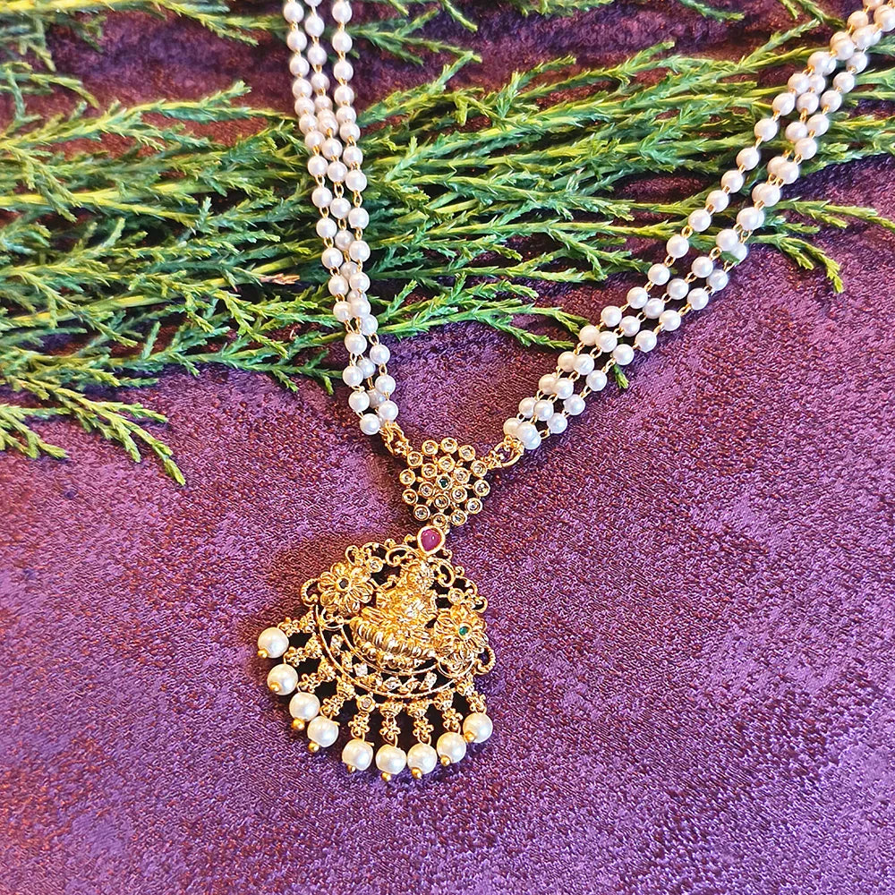 Gold necklace with pearl beads on a purple textured surface with green leaves.