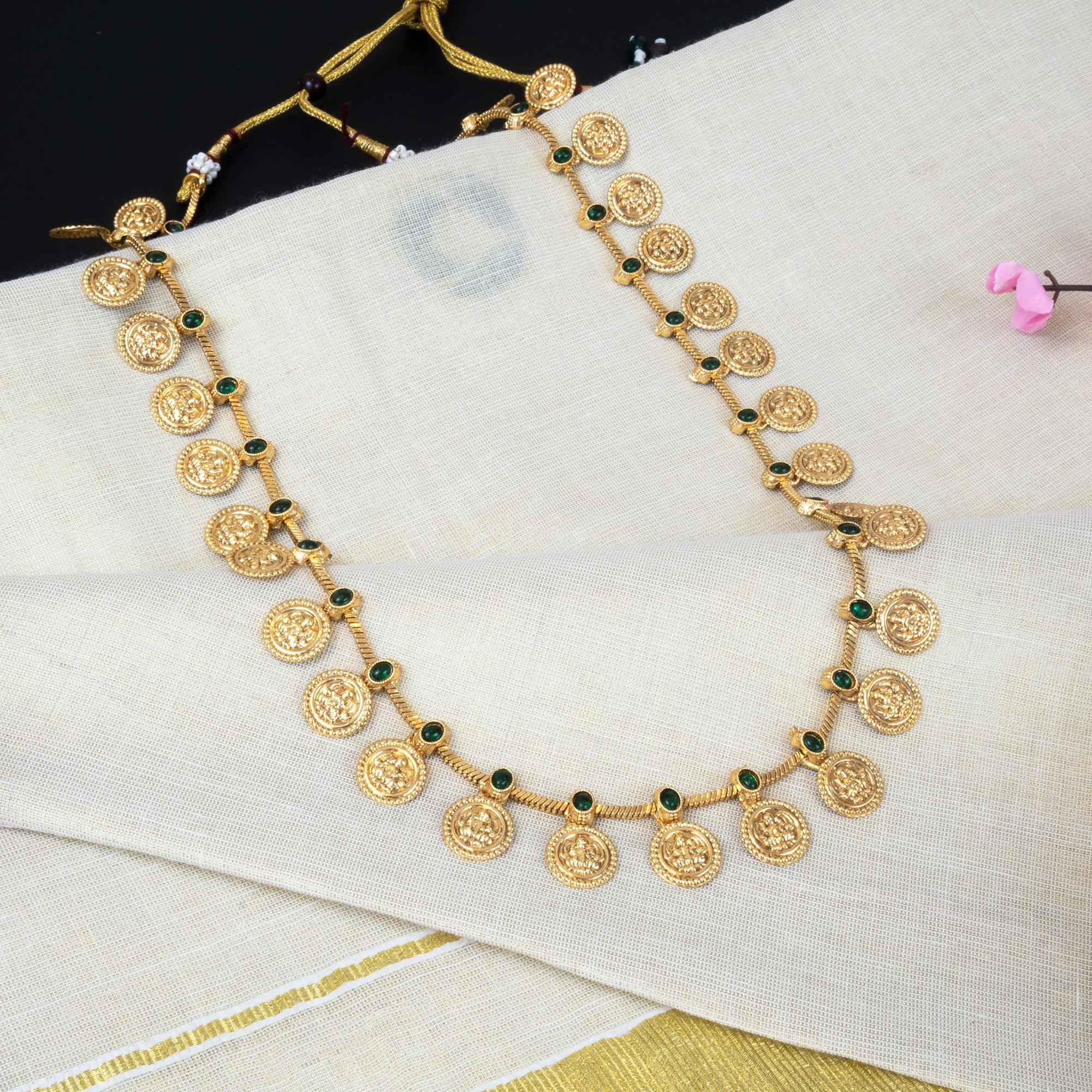 Gold necklace with green gemstones on a white fabric background