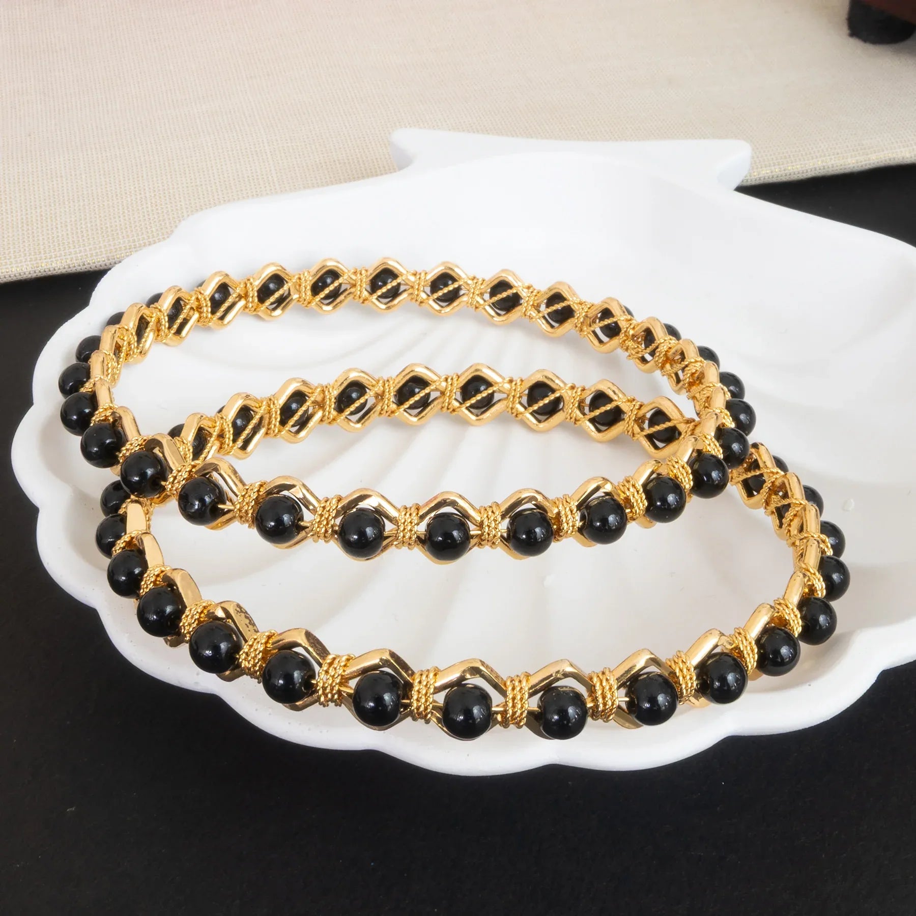 Set of black beaded bracelets with gold accents on a white shell