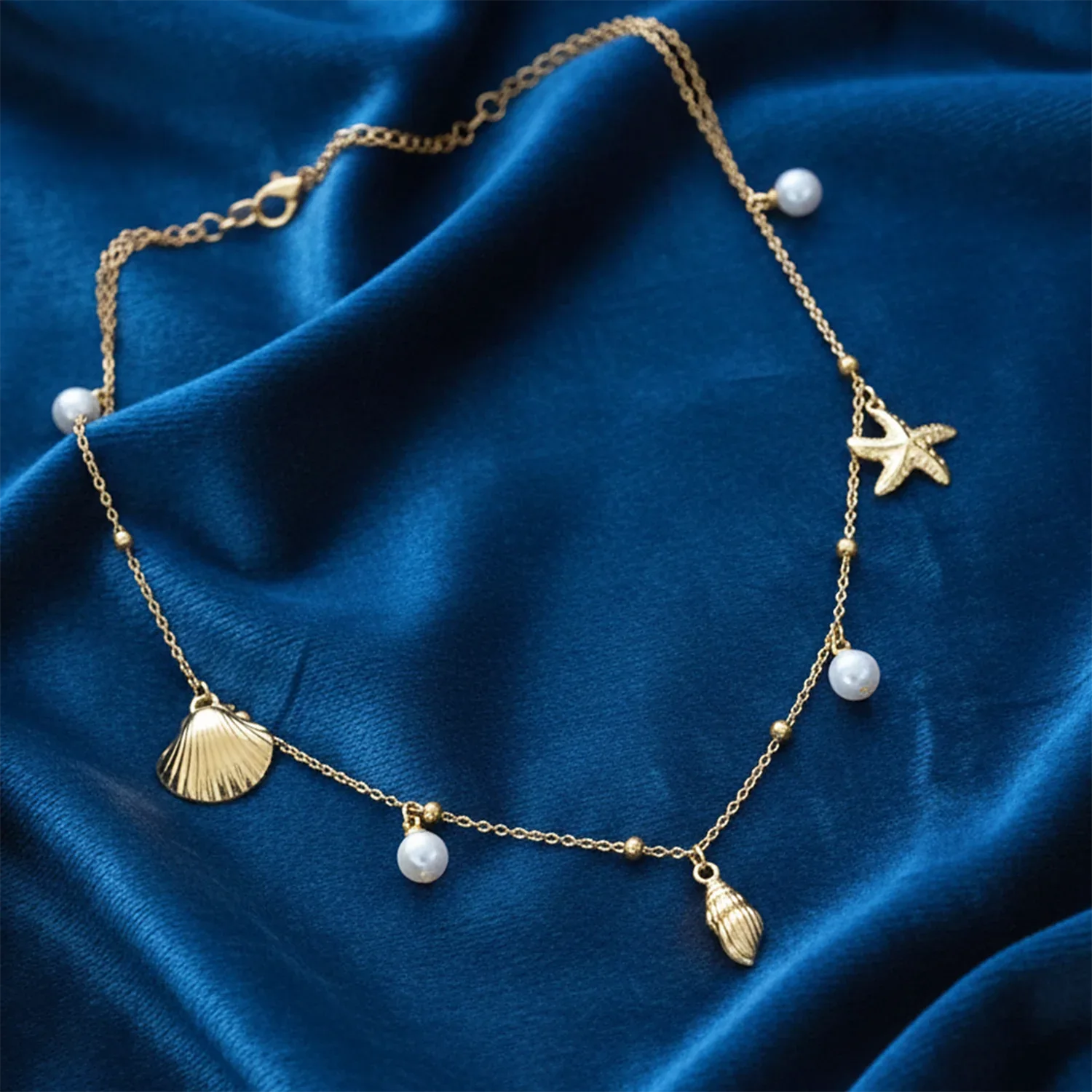 Gold necklace with shell, star, and fish charms on a blue fabric background