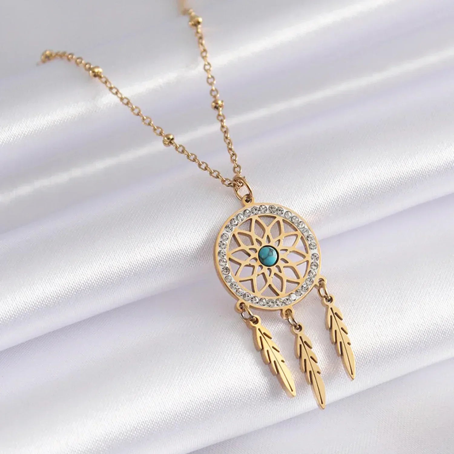 Gold necklace with a dreamcatcher pendant on a white satin background