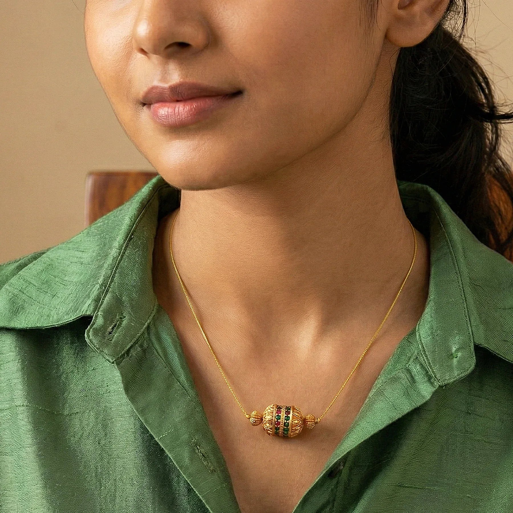 Woman wearing a gold necklace with colored beads against a neutral background