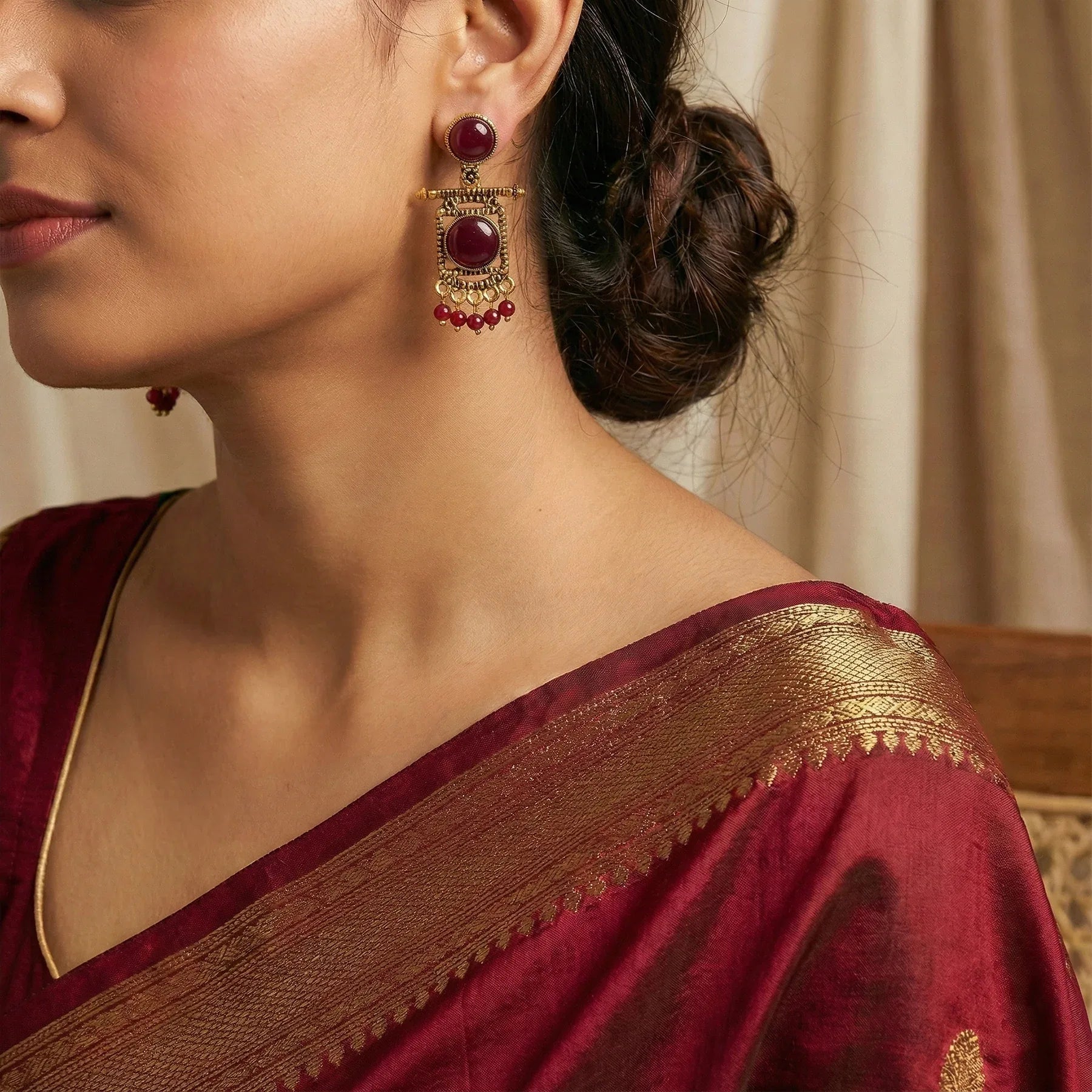 Woman wearing a maroon saree with gold border and red earrings.