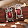 Ornate silver earrings with red stones on a wooden surface