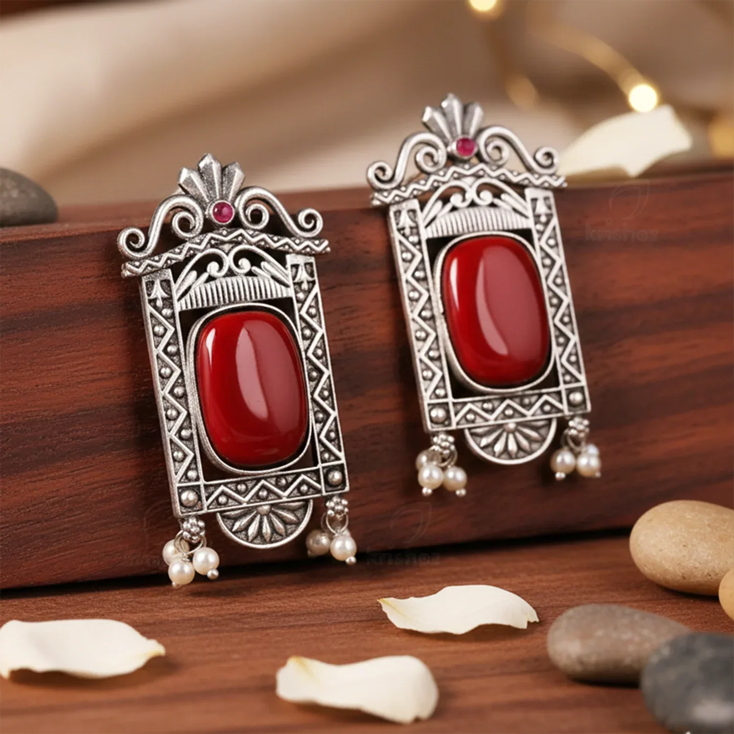 Ornate silver earrings with red stones on a wooden surface