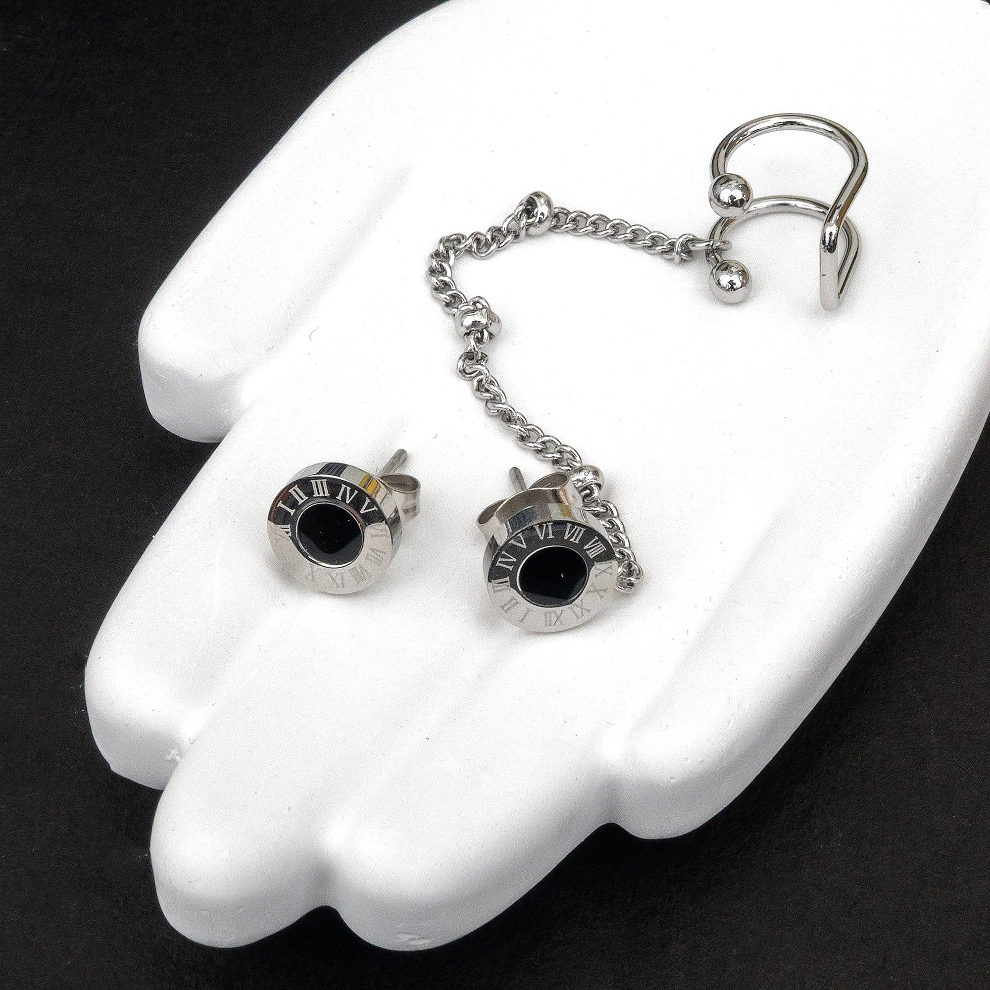 Silver earrings with black stones on a white hand model against a black background