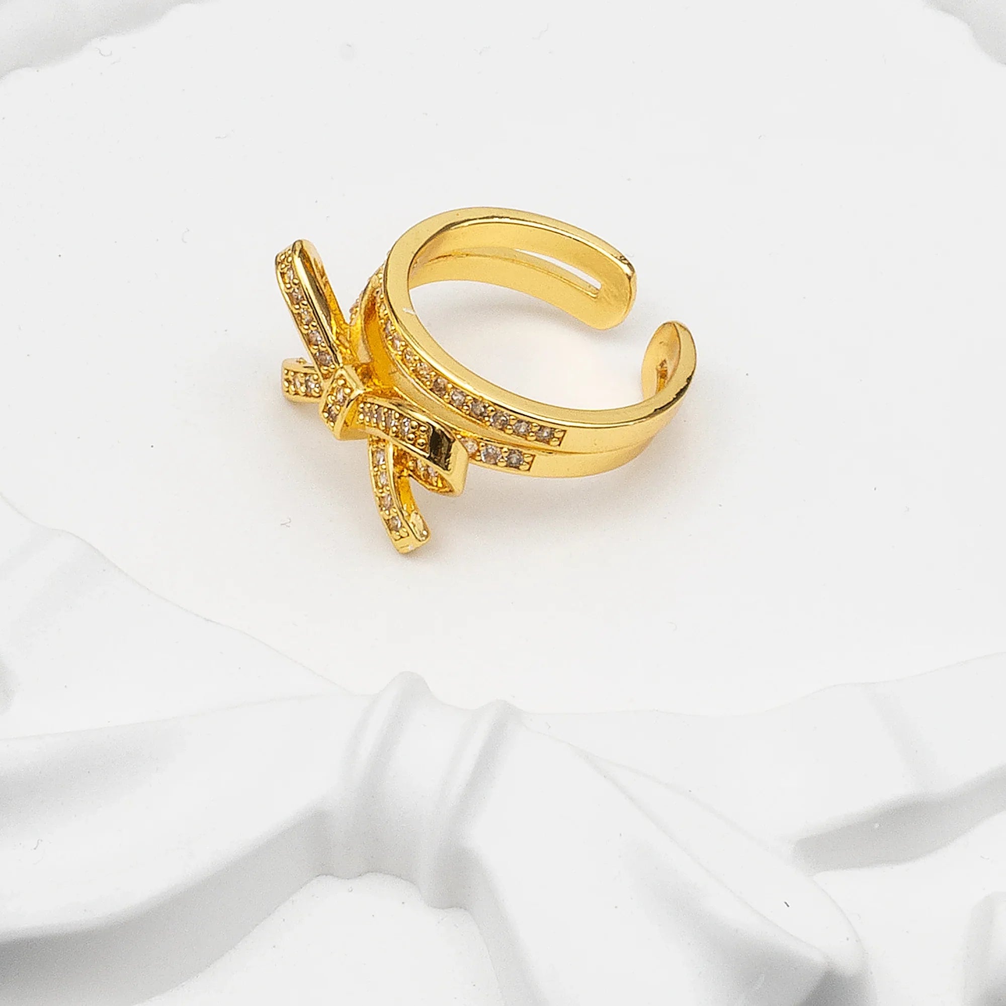 Gold bow-shaped ring with small stones on a white fabric background