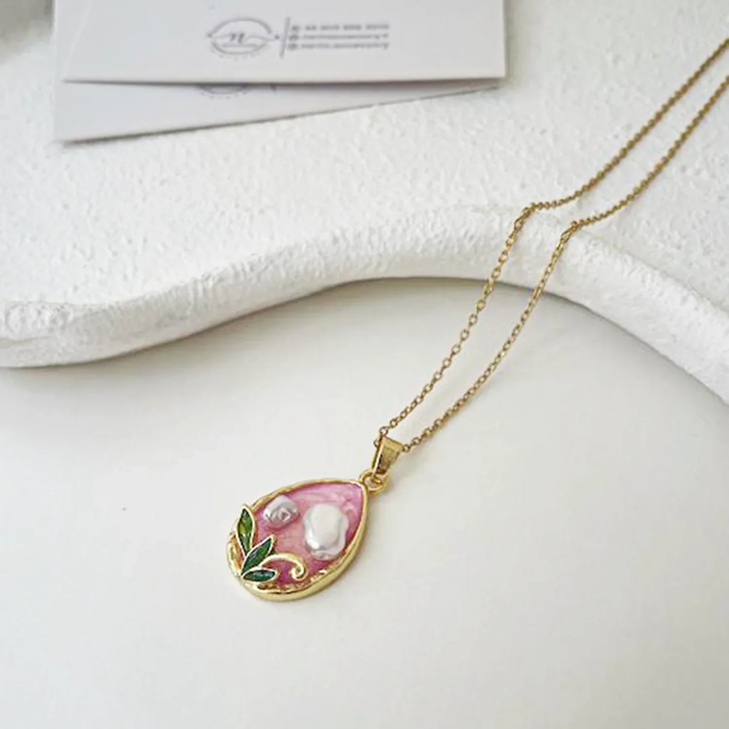 Gold necklace with a pink pendant on a white surface