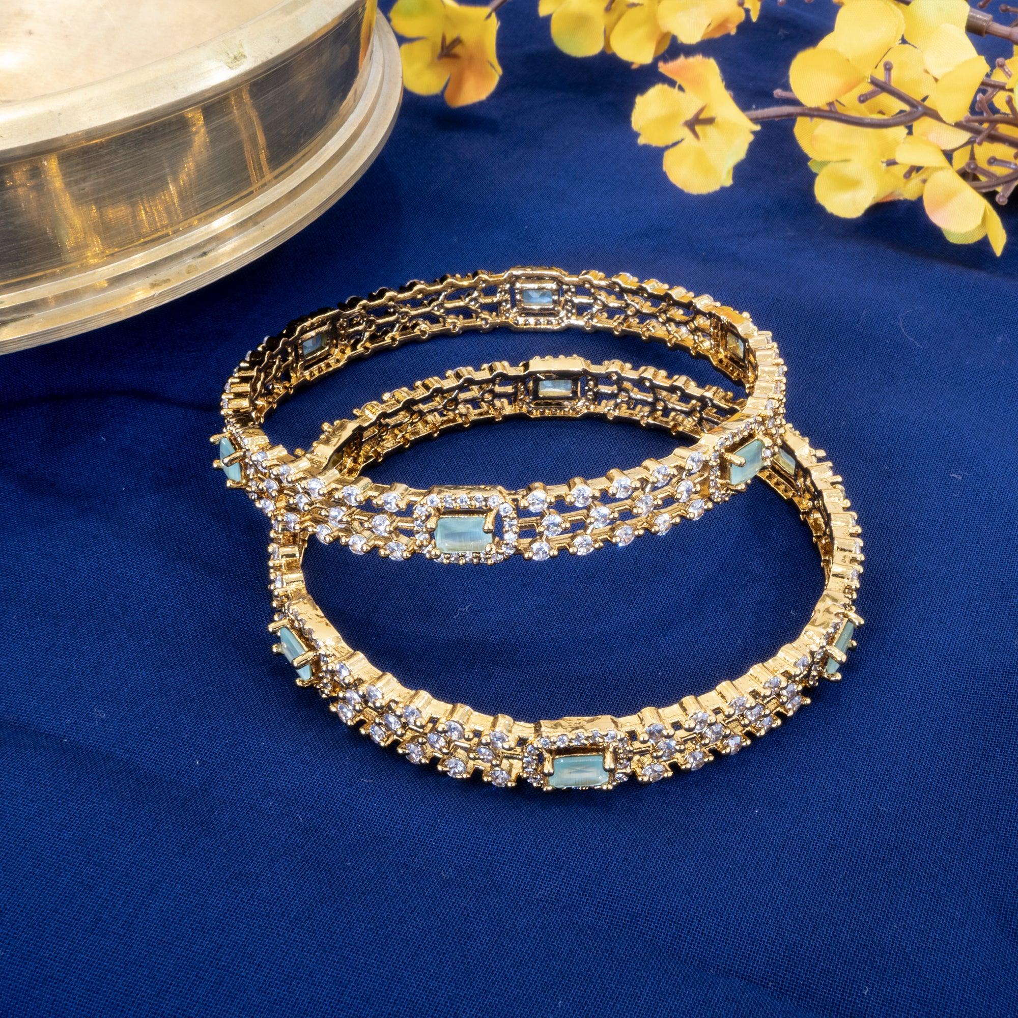 Gold bracelets with gemstones on a blue fabric background with yellow flowers.
