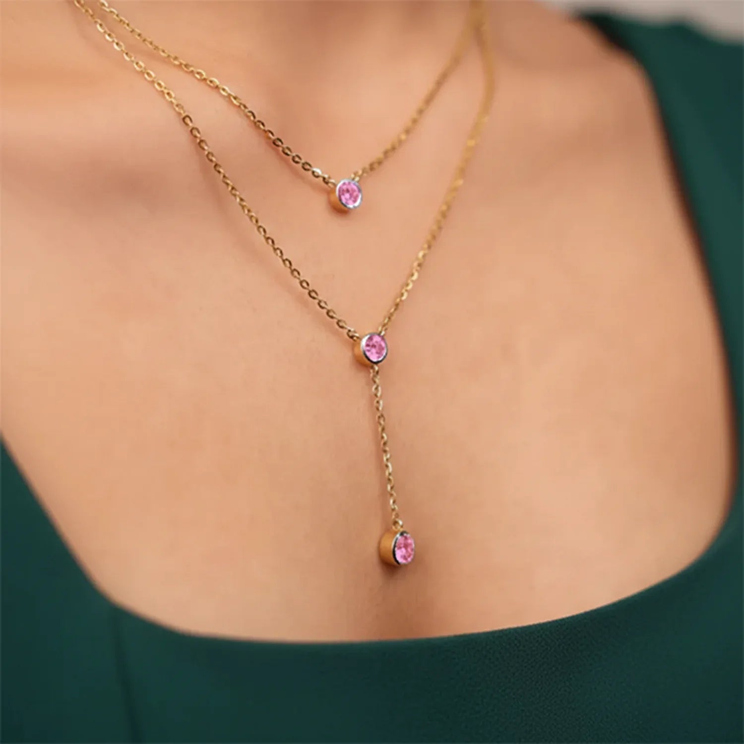Gold necklace with pink gemstones worn by a person against a green background