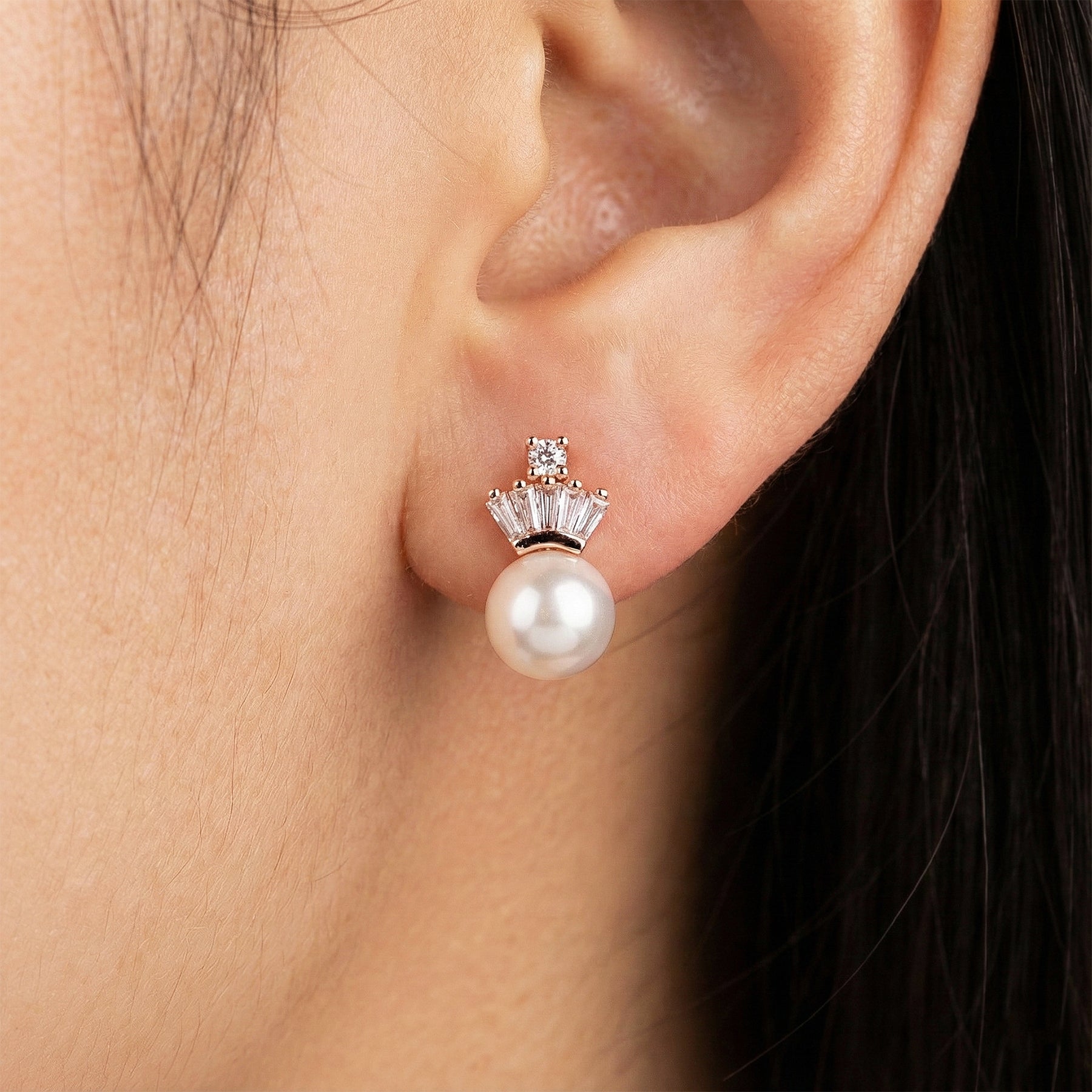 Pearl earring with a gold and diamond-like top worn by a person.
