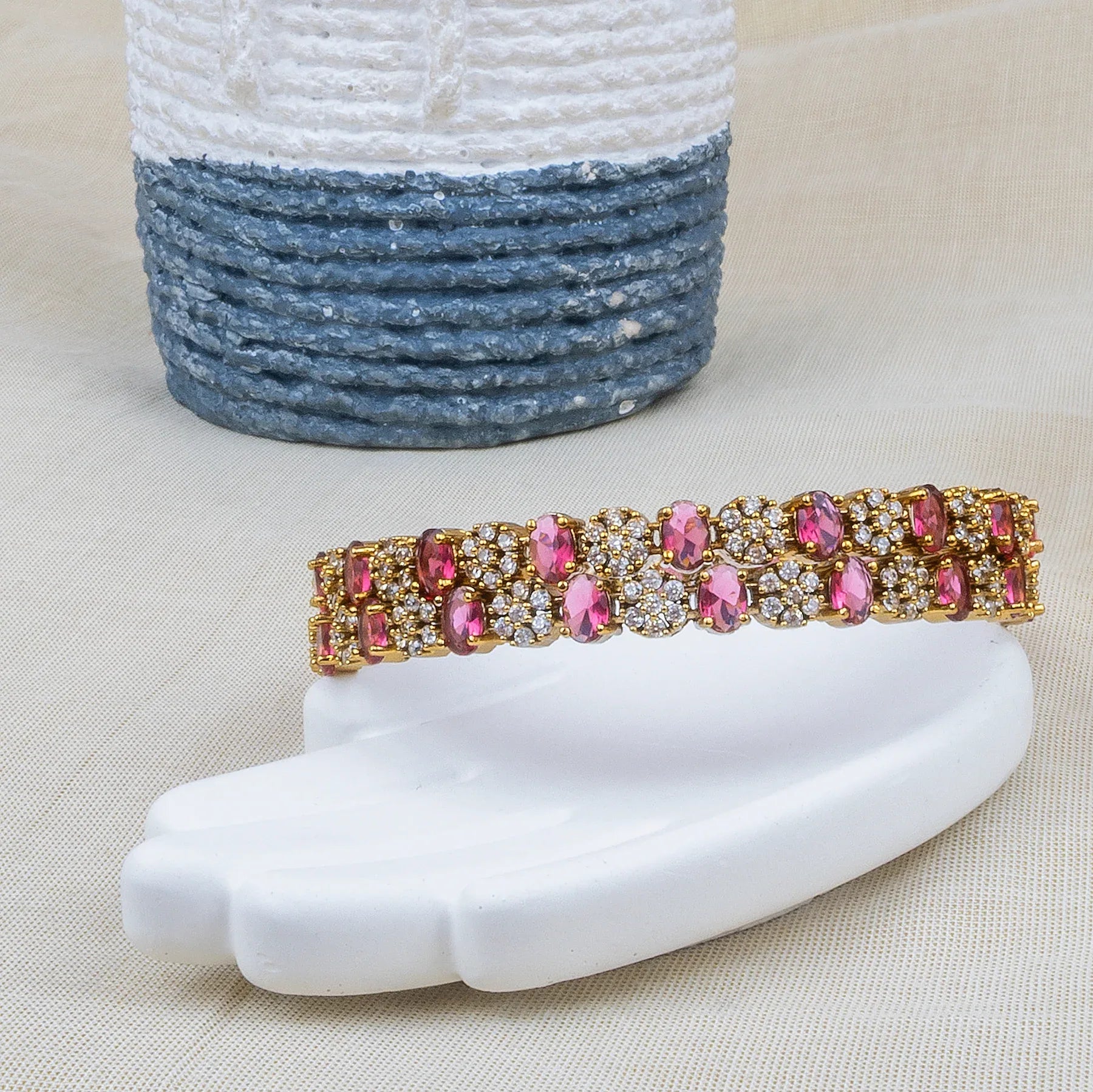 Bracelet with pink and gold stones on a white surface with a textured blue and white vase in the background.