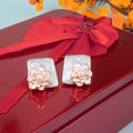 Pair of floral earrings with pearl accents on a red surface with a red bow.