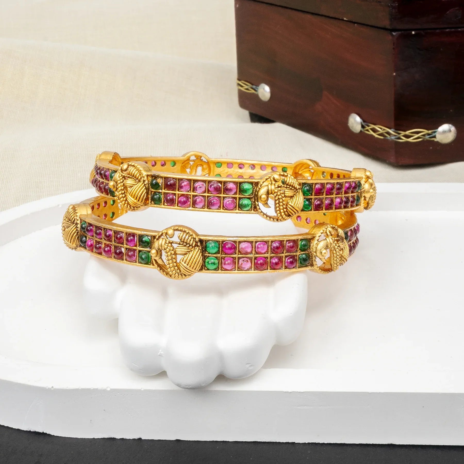 Gold bangles with colorful stones on a white surface