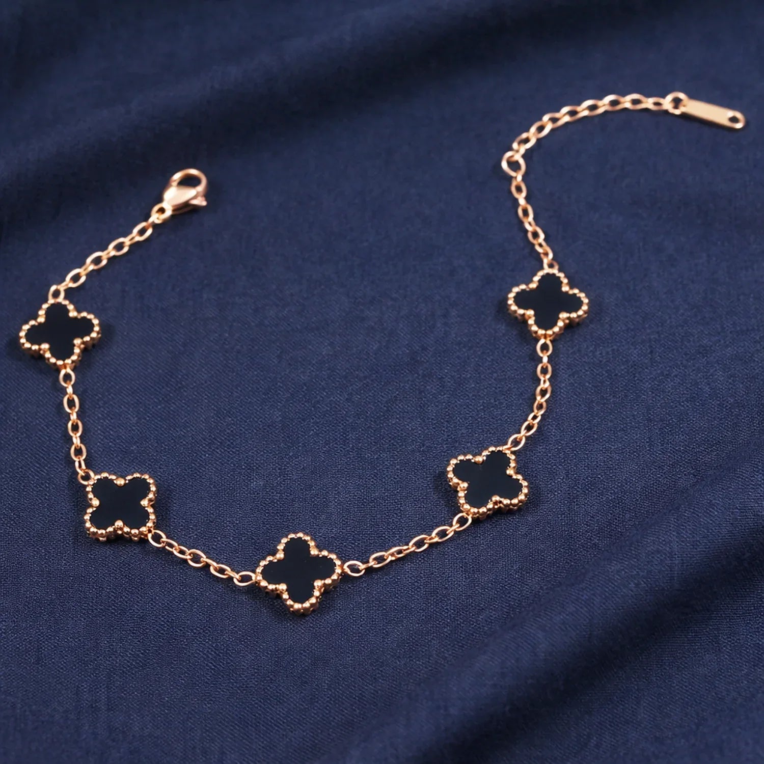 Gold bracelet with clover-shaped links on a blue fabric background